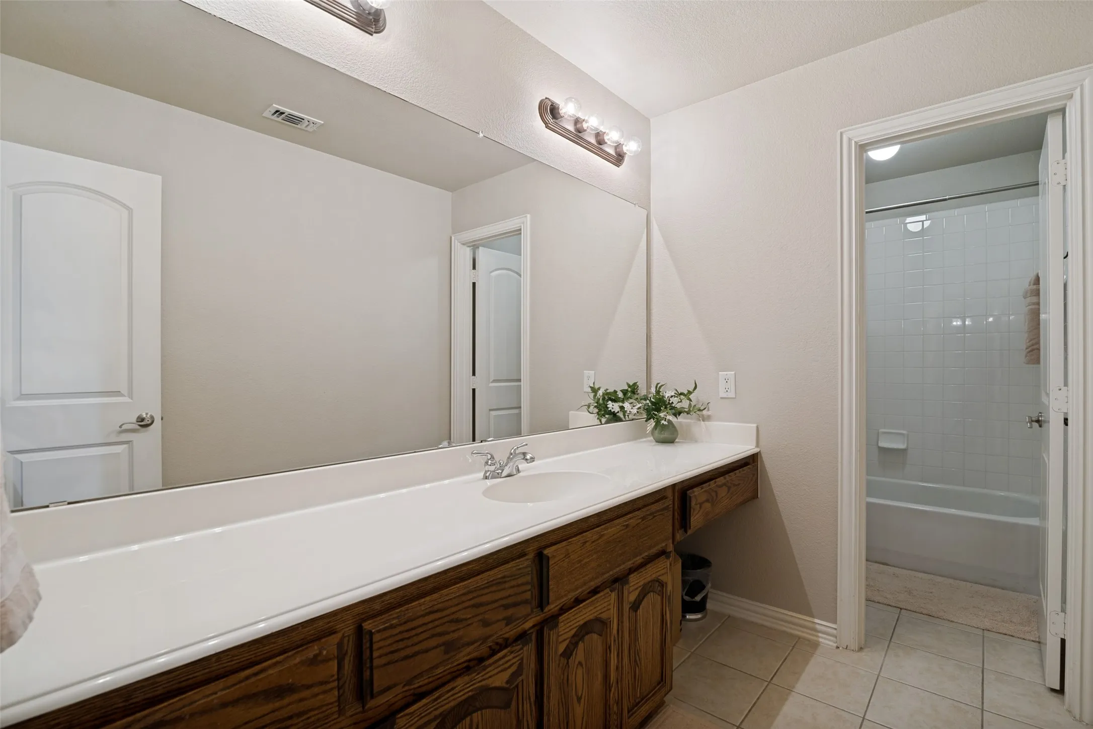 Spacious bathroom featuring a long wood-finish vanity with a single basin, a large wall-mounted mirror, and tile flooring