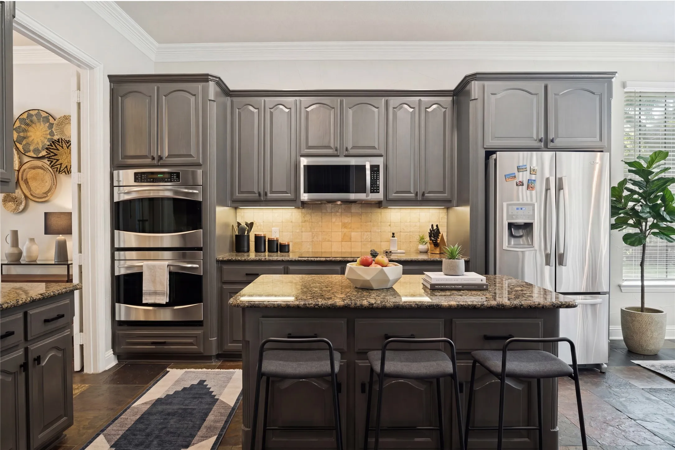 Kitchen featuring dark cabinetry, stainless steel appliances, a built-in double oven, a kitchen island with seating, and stone countertops