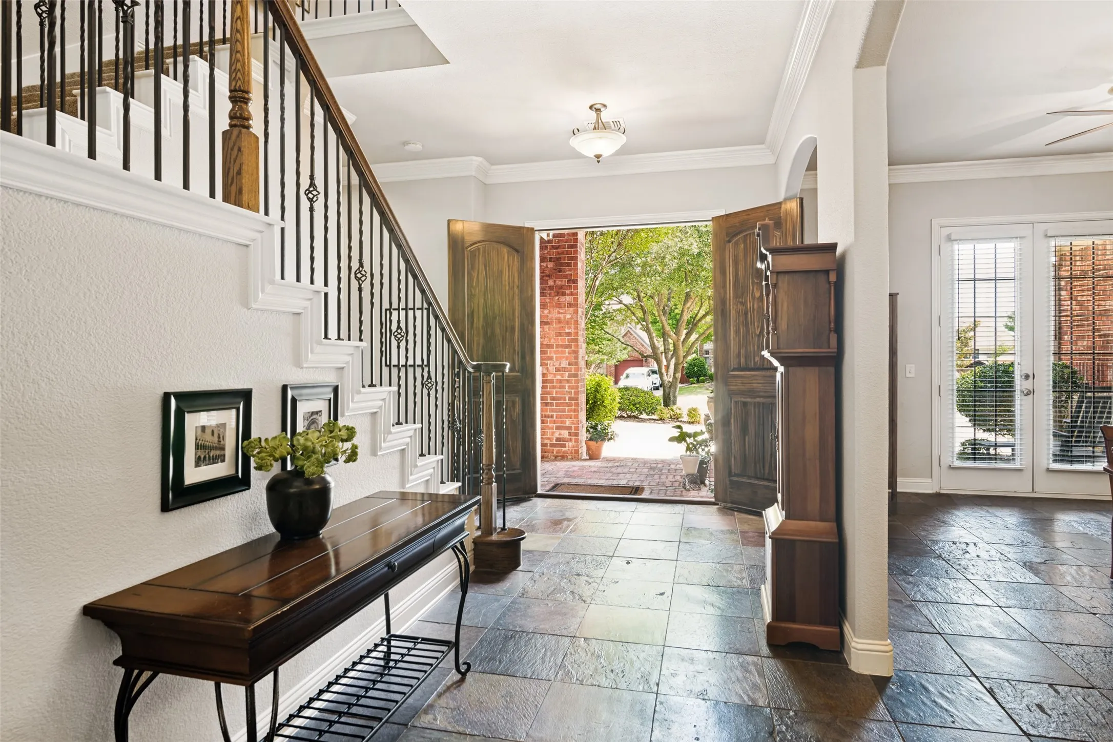Foyer featuring slate tile flooring, a staircase with wrought iron balusters and wood handrail, double front doors, and an arched entry