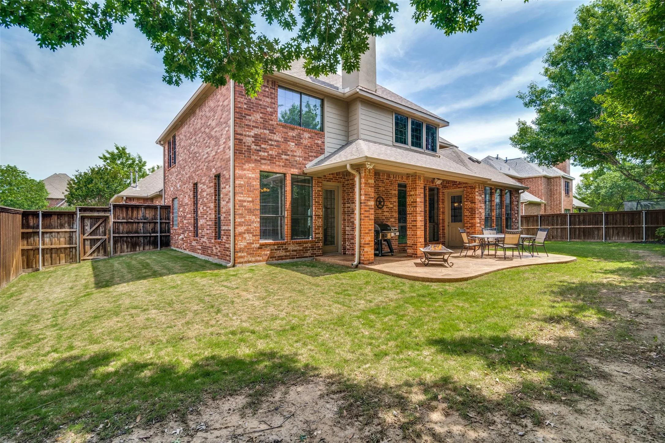 Brick exterior featuring a covered patio, shaped concrete hardscape, and a fenced backyard