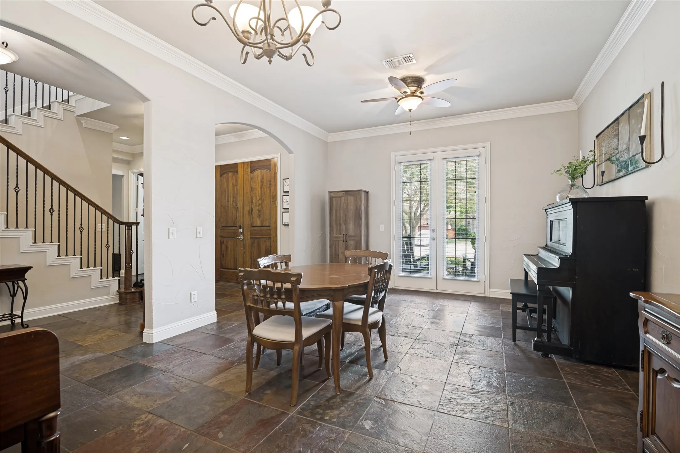 Spacious room featuring multi-toned stone tile flooring, crown molding, and a chandelier lighting fixture