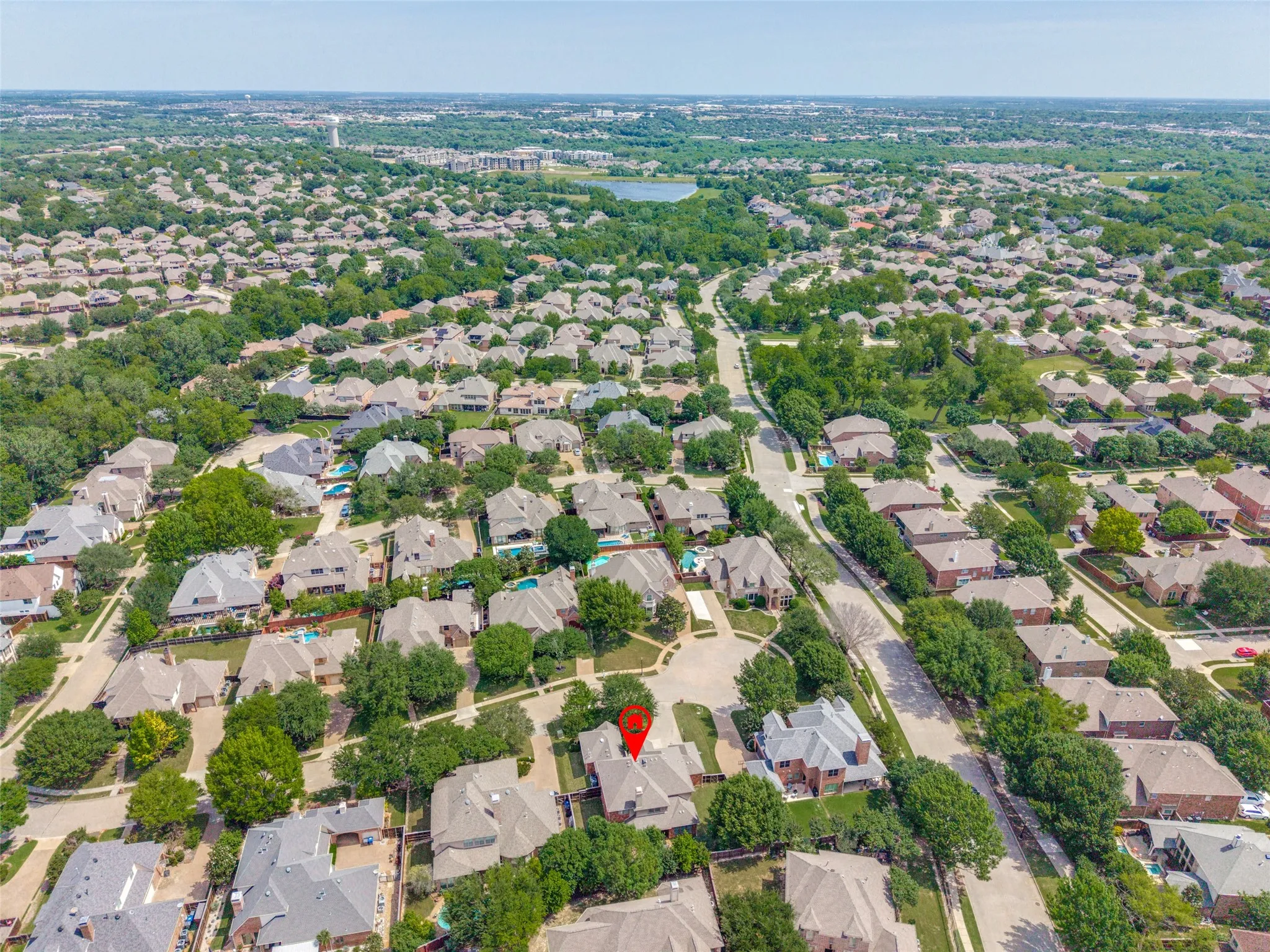 Aerial perspective of a residential neighborhood with numerous single-family homes, mature trees, and a distant body of water
