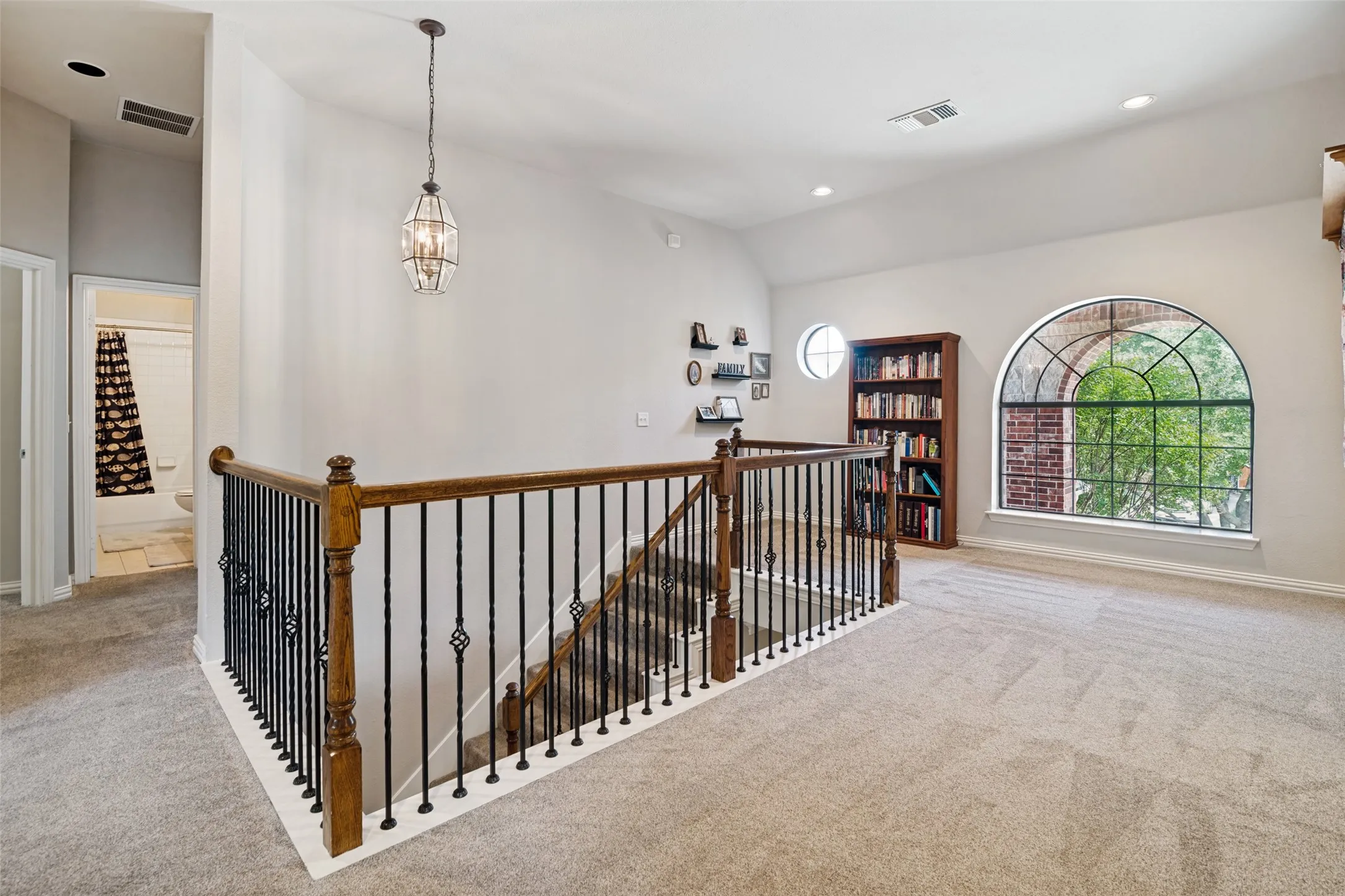 Spacious landing area featuring a decorative wrought iron and wood baluster, vaulted ceilings, a large arched window with grid detailing, and recessed lighting
