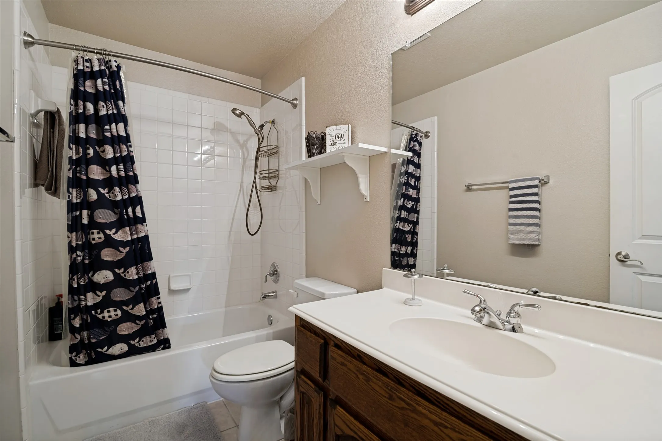 Full bathroom featuring a white tub-shower combination with subway tile surround, a dark wood-finish vanity with a white integrated sink, a large wall-mounted mirror, and neutral wall paint