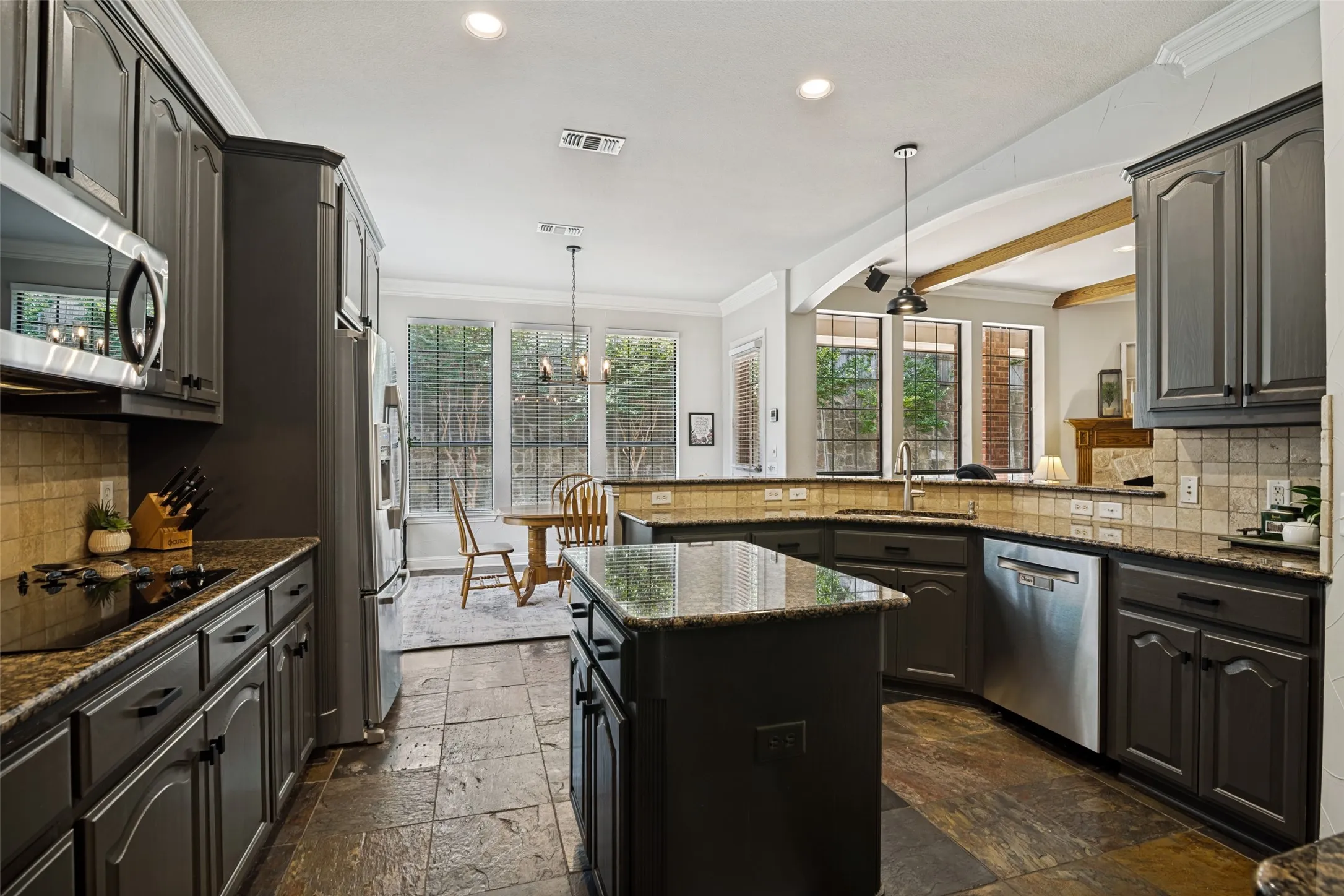 Kitchen featuring dark cabinetry, granite countertops, stainless steel appliances, a central island, and stone tile flooring