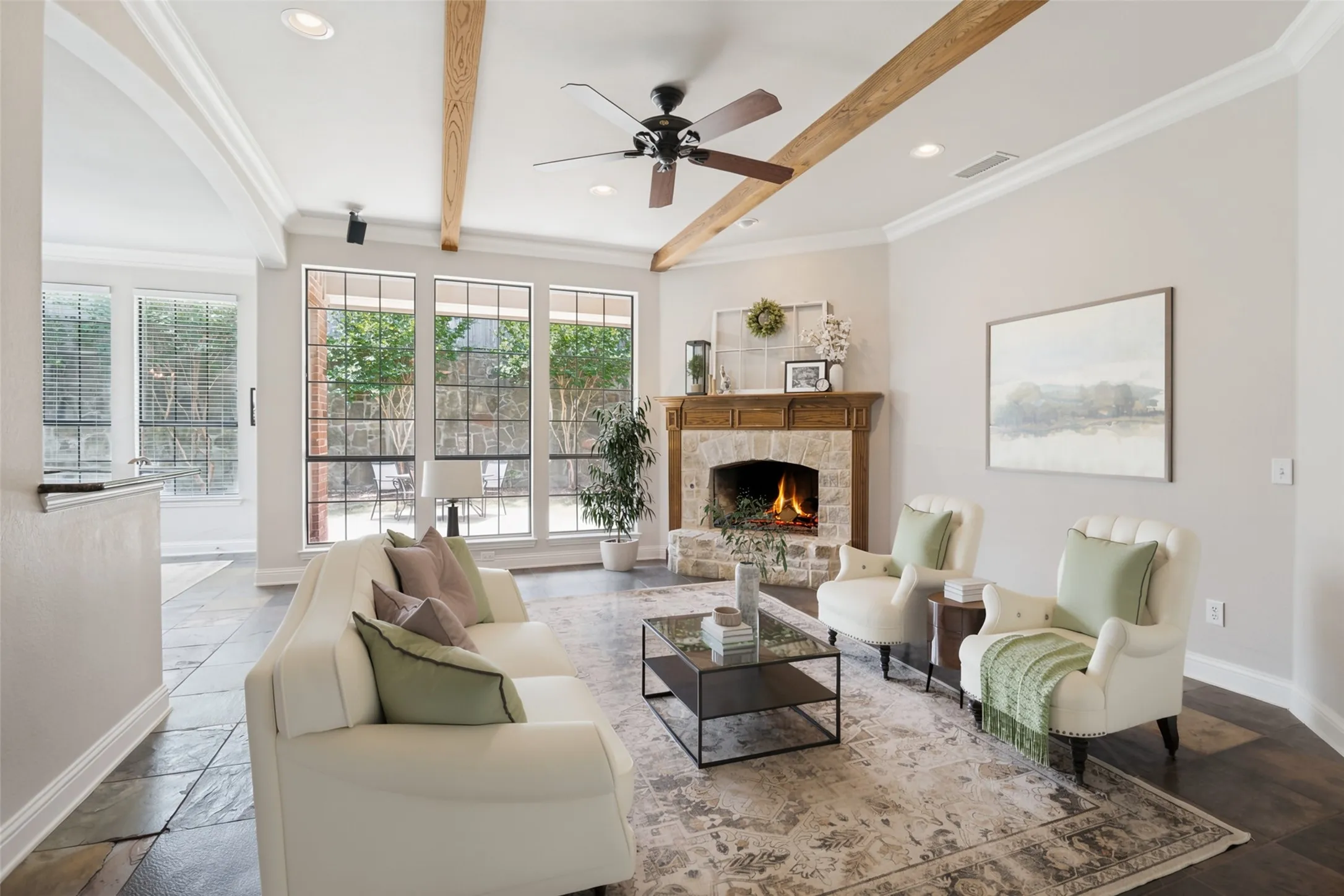 Virtually staged. Spacious living area featuring a stone-clad fireplace with a wood mantle, exposed wood ceiling beams, and recessed lighting