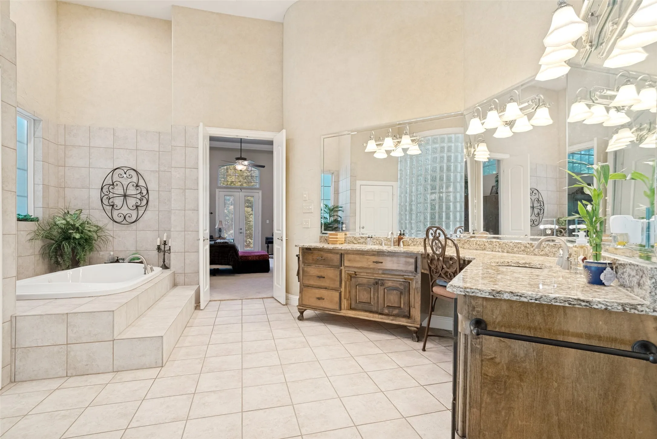 Spacious bathroom featuring a built-in jetted tub with tile surround, dual vanity with granite countertops, wood-finish cabinetry, and extensive mirror lighting