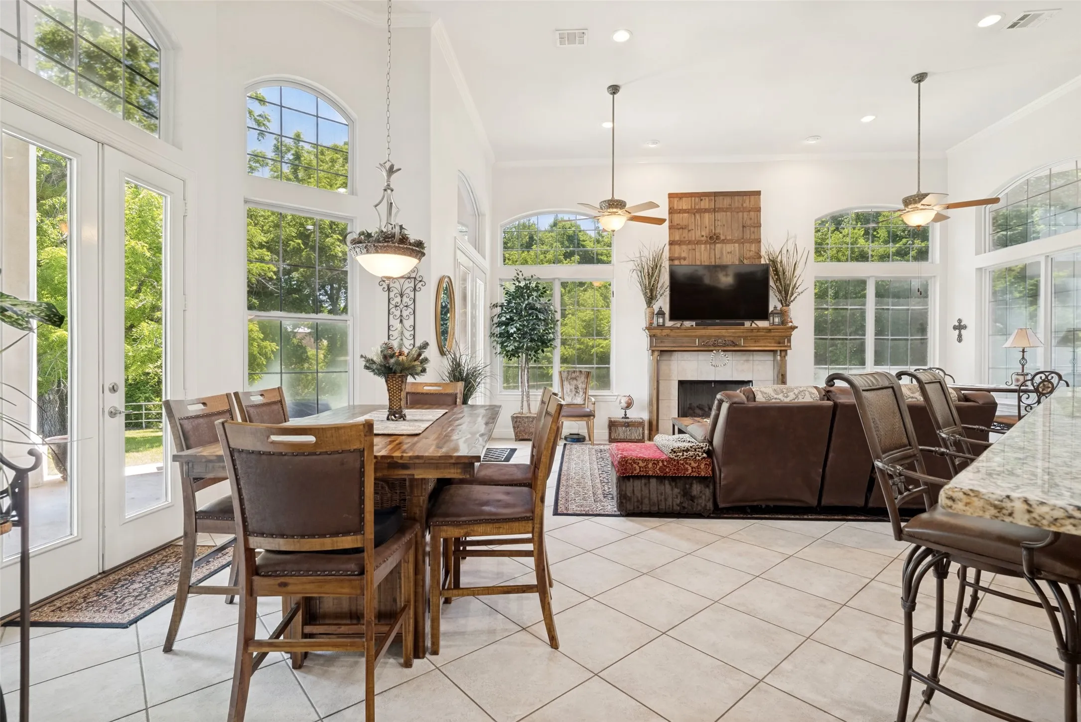 Spacious interior featuring high ceilings, extensive arched and rectangular windows, white tile flooring, a fireplace with a detailed mantel, and recessed lighting