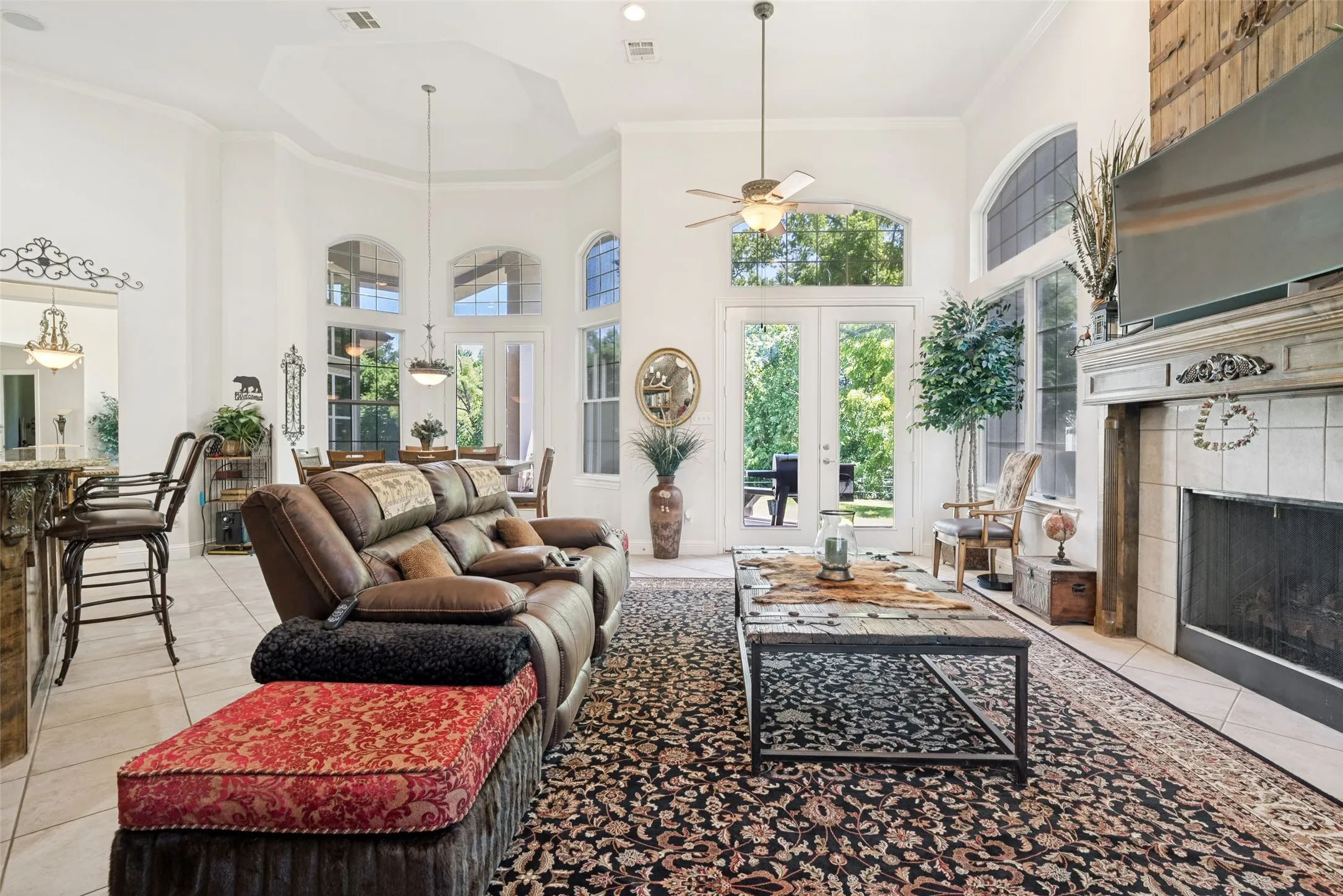 Spacious interior featuring a fireplace with a decorative mantel, high ceilings, multiple arched windows, French doors, and tile flooring