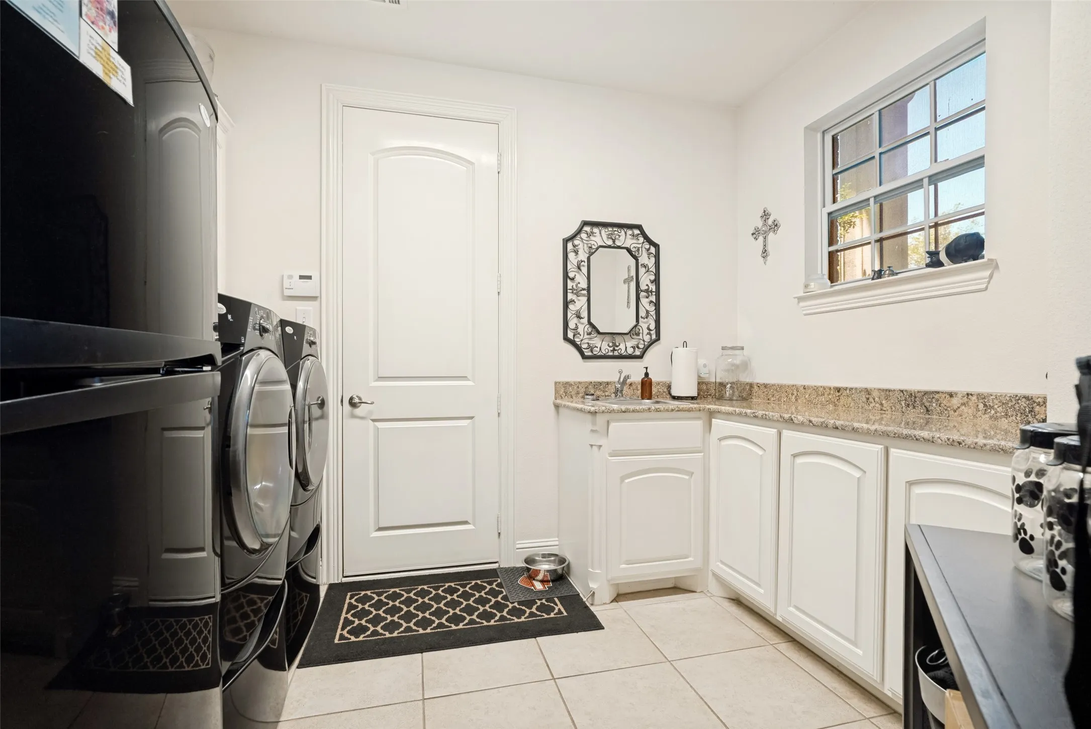 Utility room featuring white shaker-style cabinetry, a built-in sink, granite-style countertops, and tile flooring