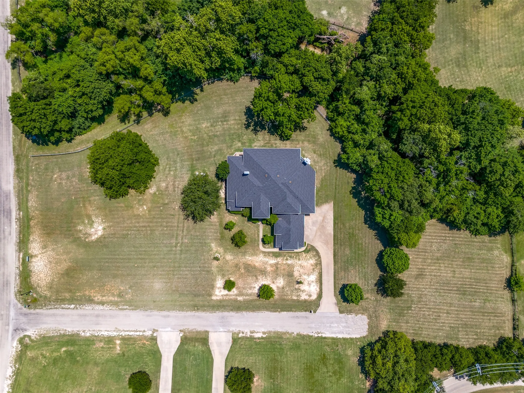 Aerial view highlighting a single-story residence with a dark shingle roof, surrounded by expansive green space and mature trees