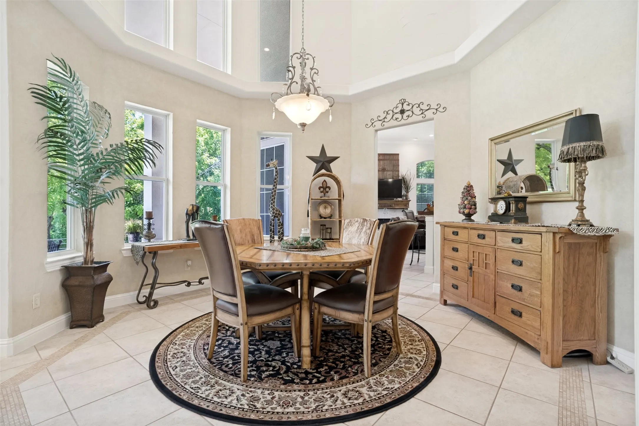 Dining area featuring light-toned tile flooring, tall windows, and a tray ceiling with a chandelier