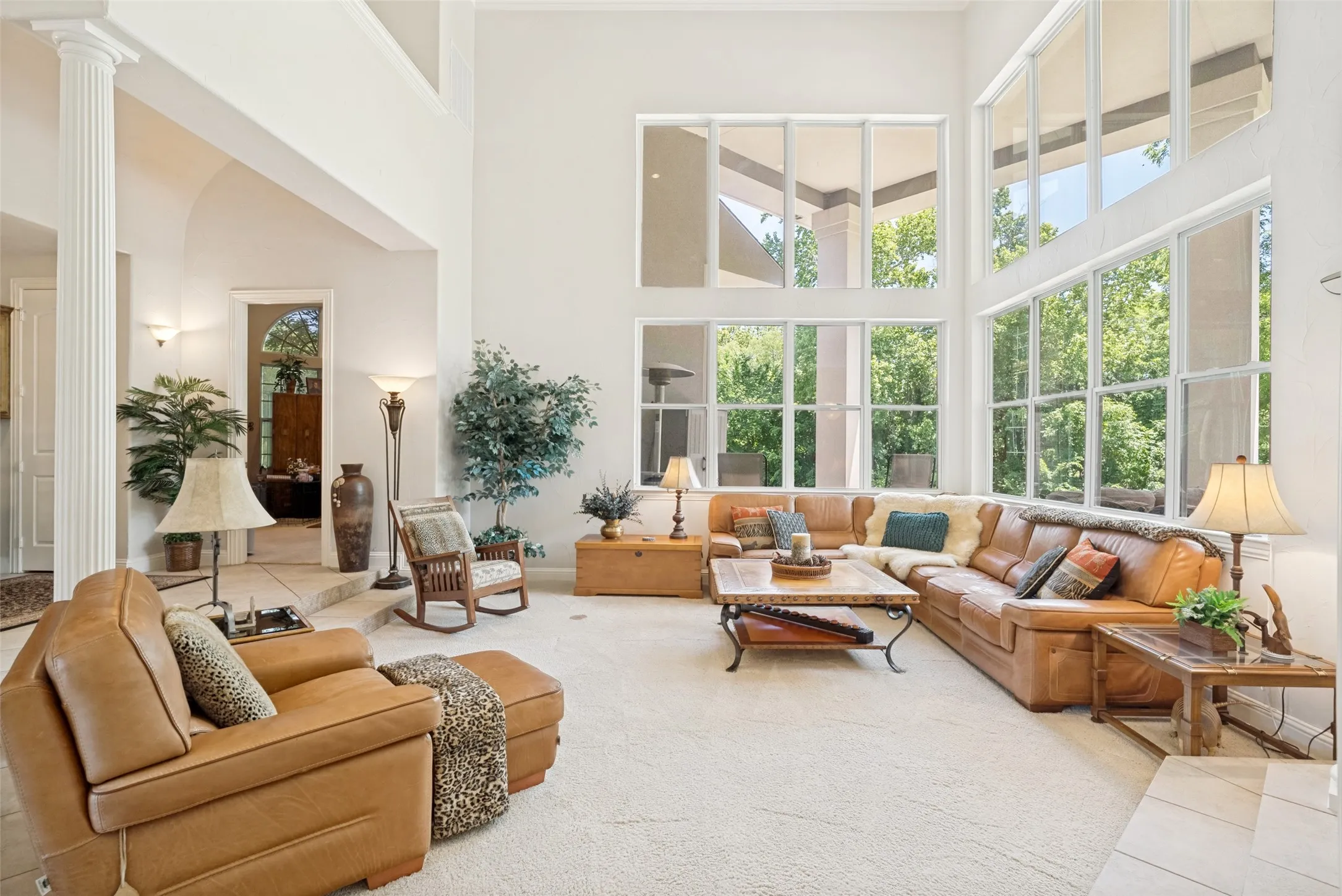 Grand living area featuring a two-story ceiling, extensive window array, light-toned carpet flooring, a decorative column, and an arched entry