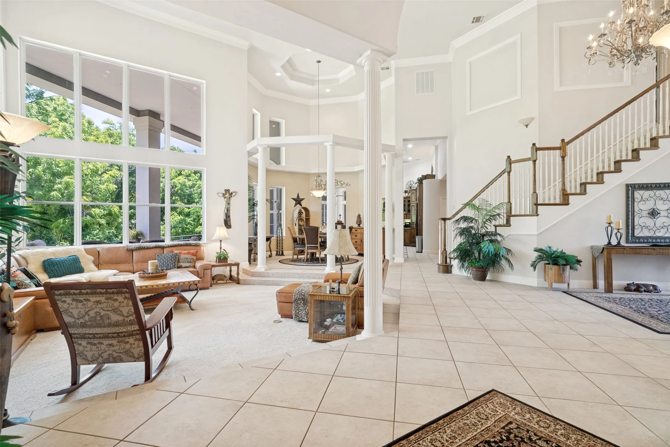 Grand entry foyer with tile flooring leading to a living area featuring a two-story window wall, high ceilings, and an elegant staircase with wood handrails