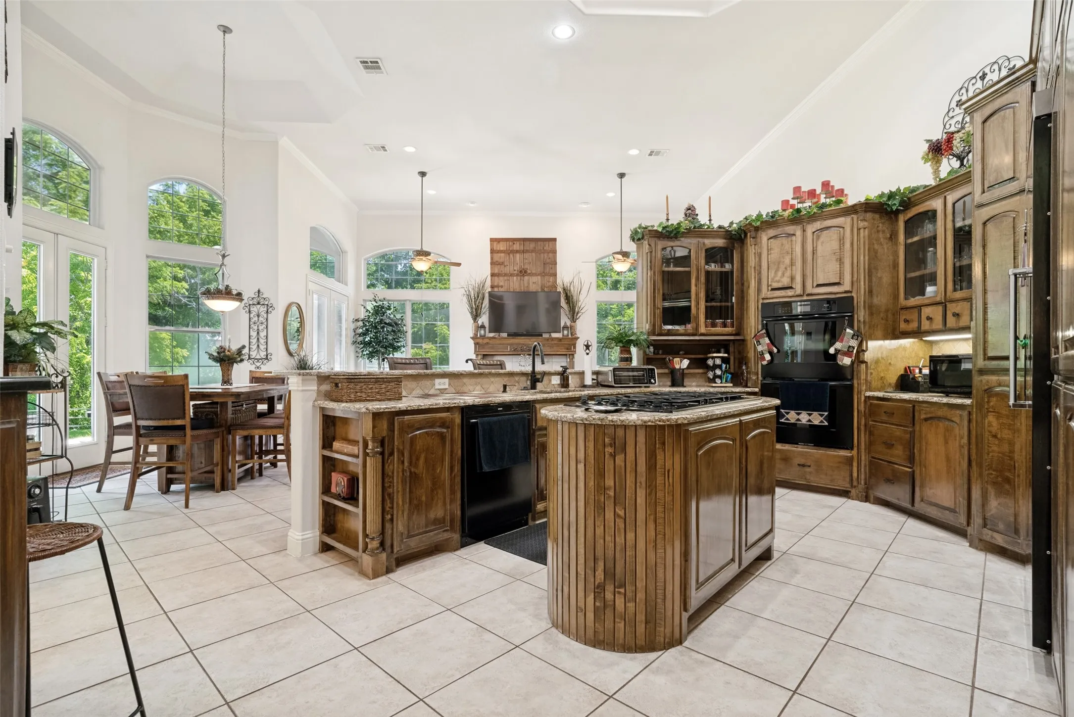 Gourmet kitchen featuring custom wood cabinetry, a central island with a built-in cooktop, granite countertops, double wall ovens, and tile flooring