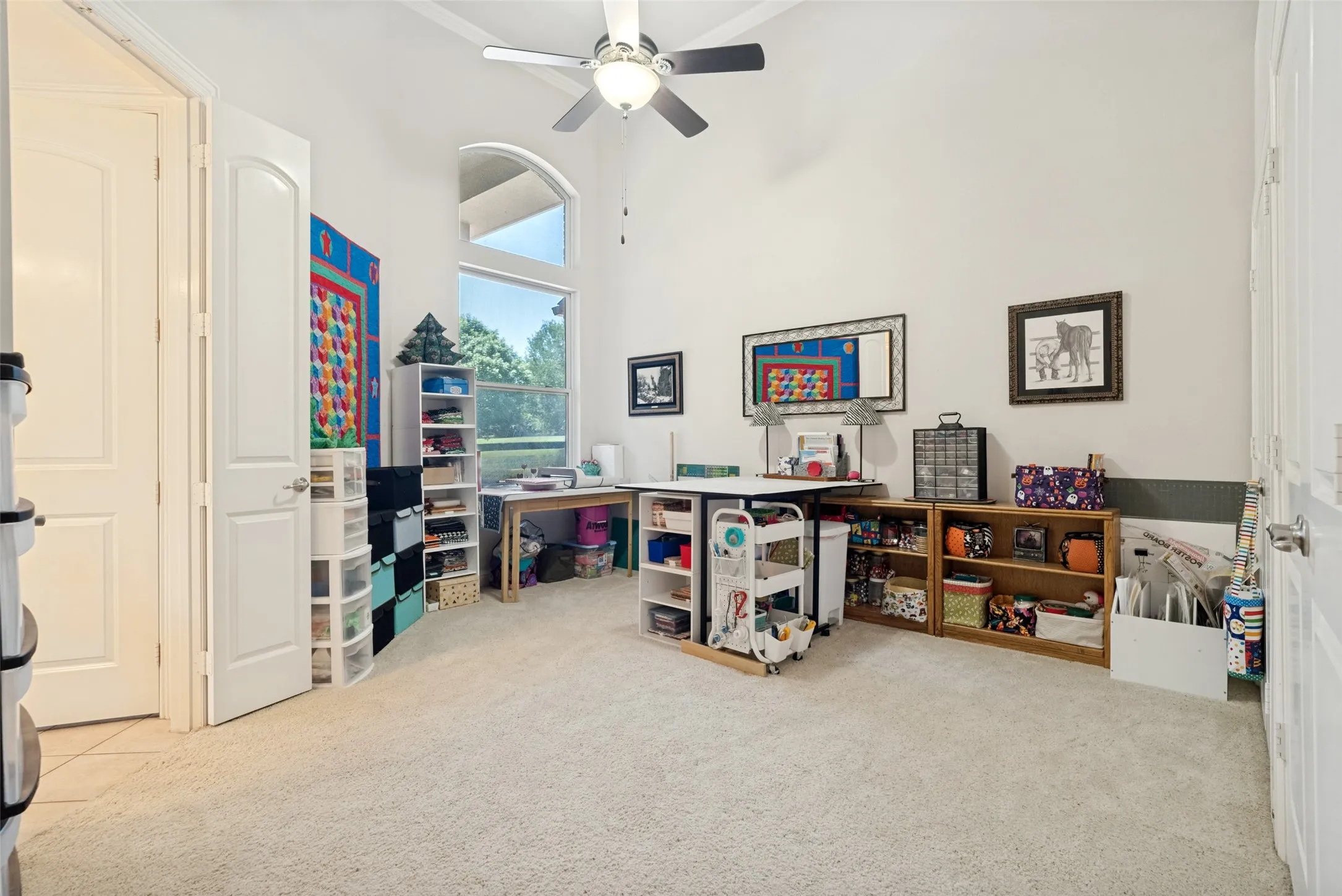 Spacious room featuring vaulted ceilings, a large arched window, a ceiling fan, and light-toned carpeting