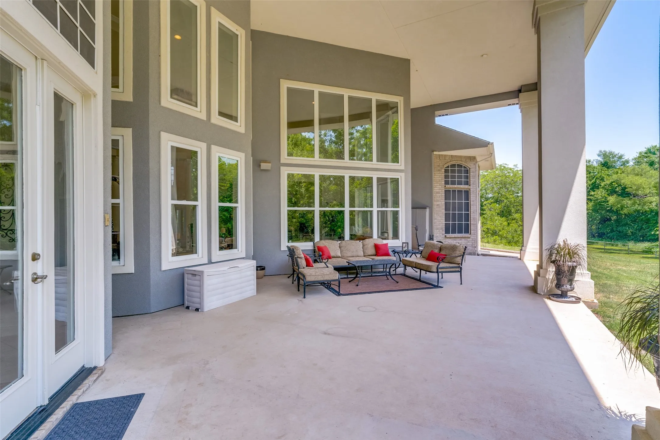 Expansive covered patio featuring a concrete surface, white trim double doors, and a wall of windows