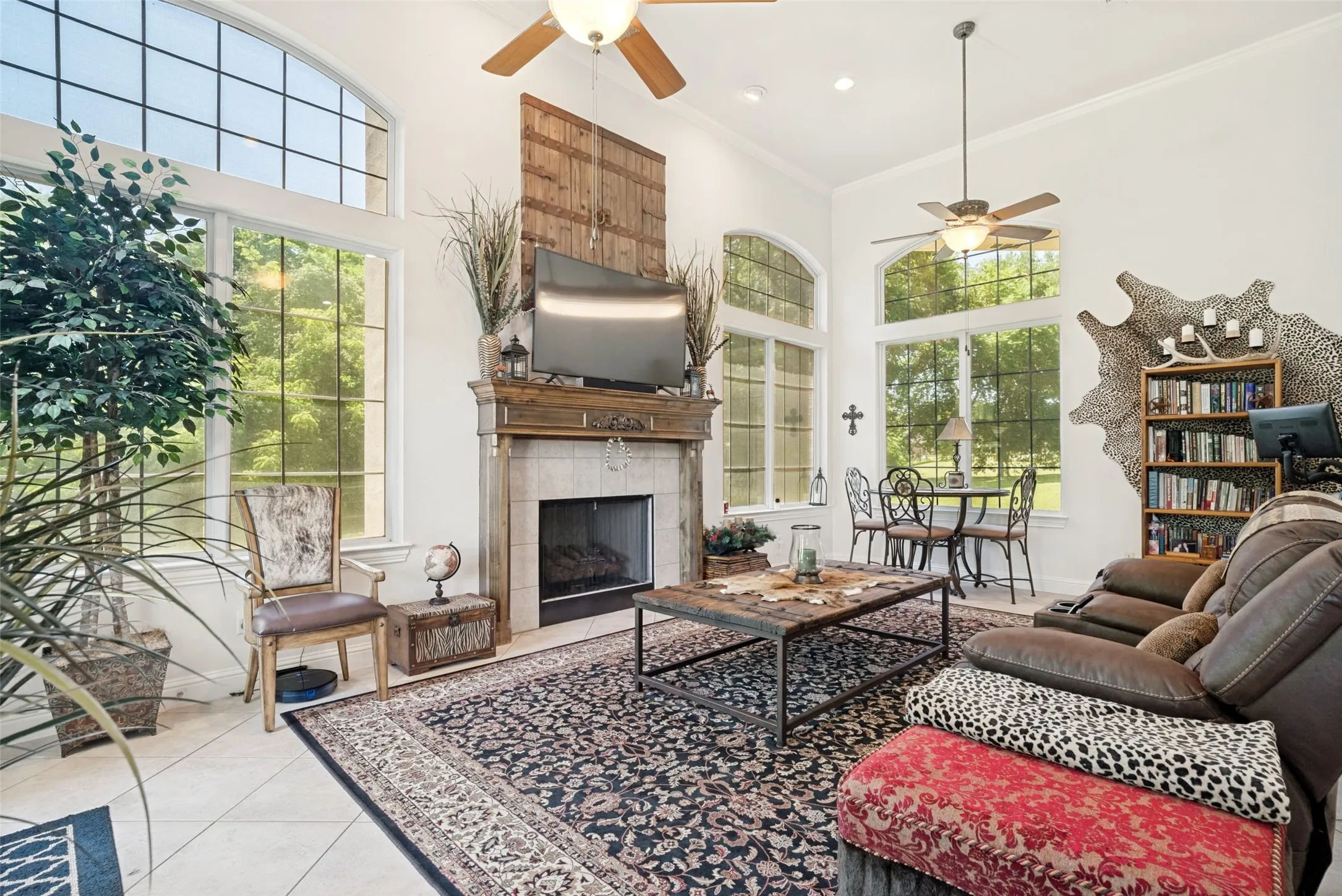 Spacious living area featuring high ceilings, large arched windows, a fireplace with a wood mantle and tile surround, recessed lighting, and tile flooring