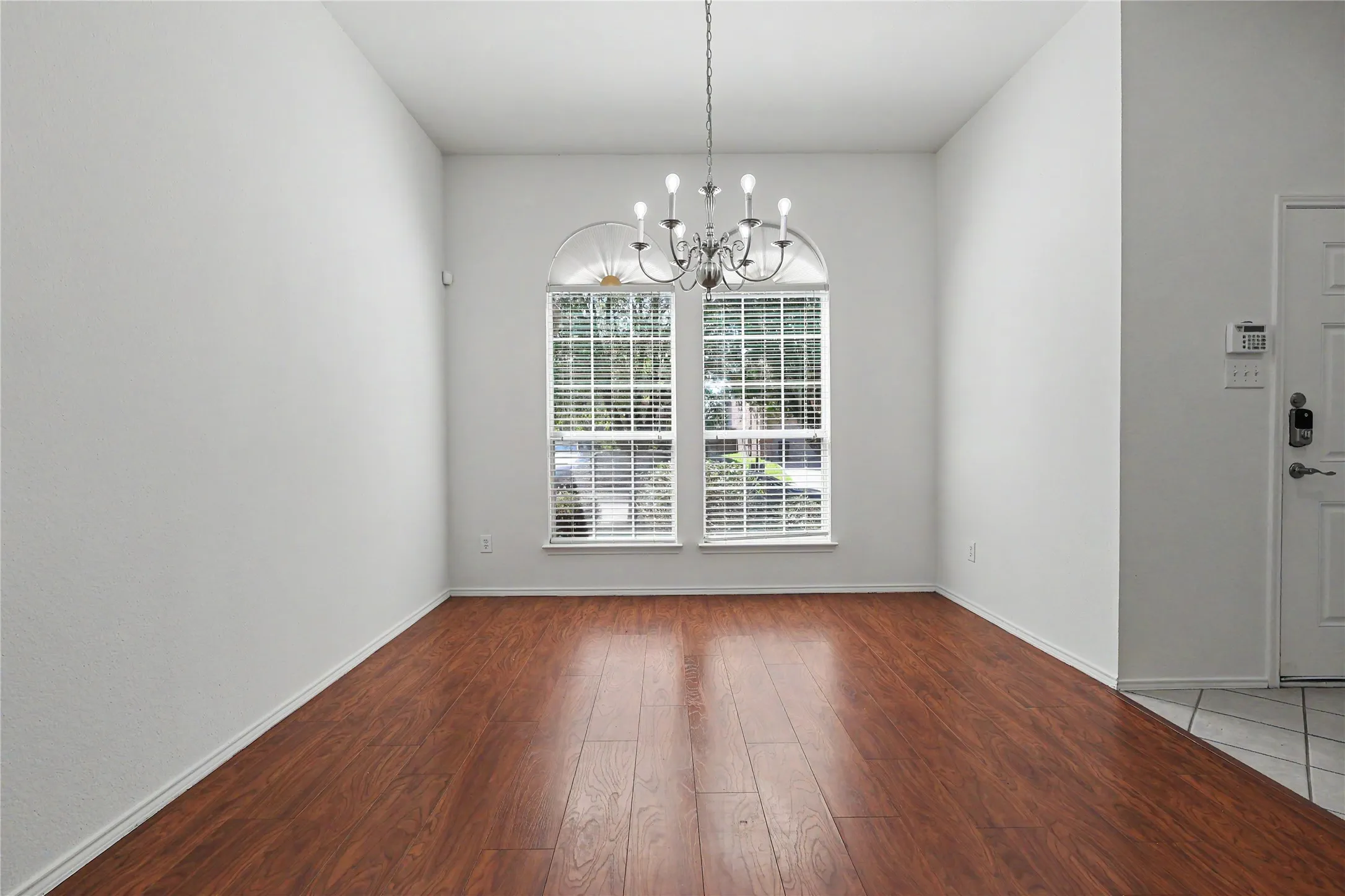Bright room featuring two arched top windows with blinds, wood-finish flooring, a classic chandelier, and white baseboards