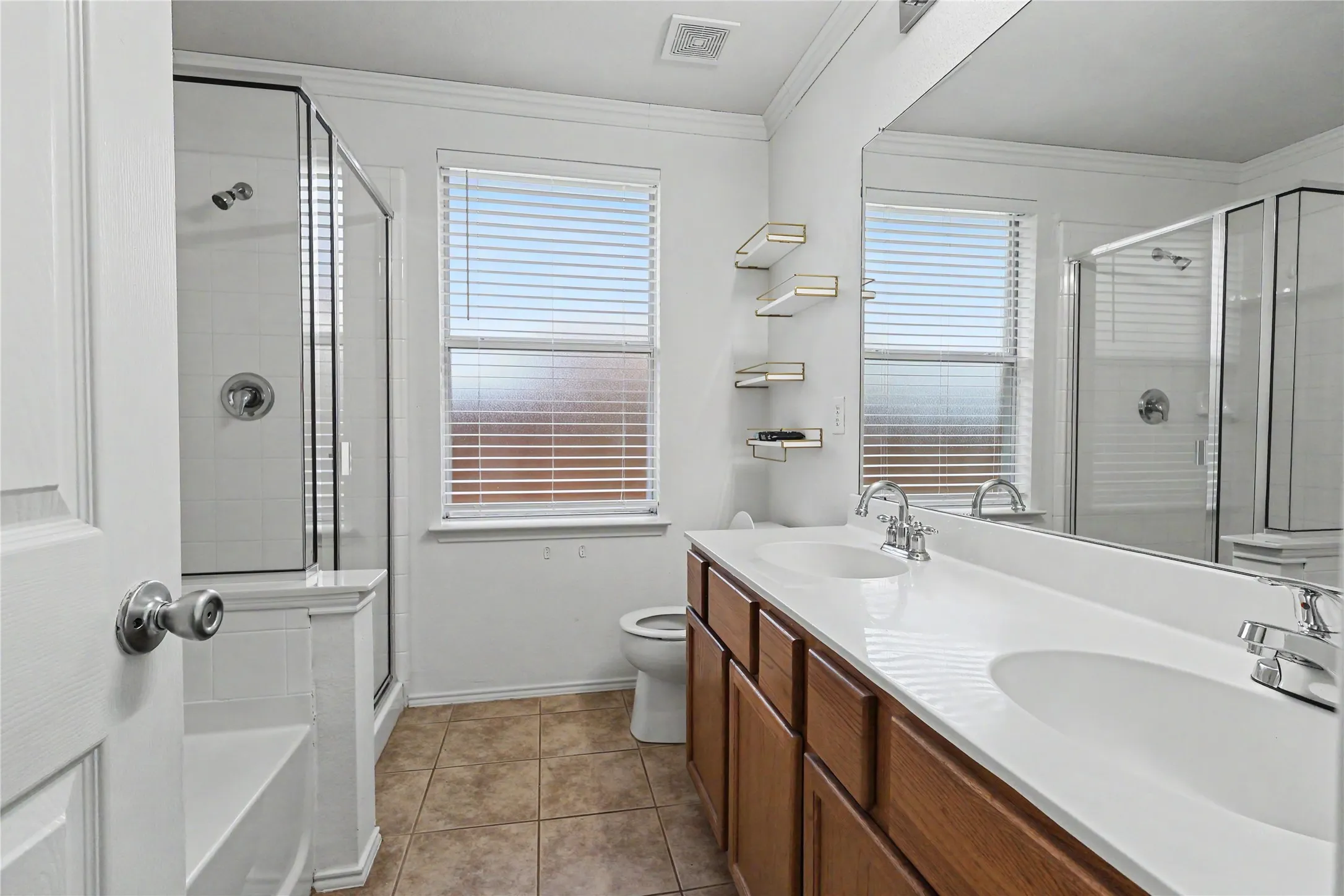 Bathroom featuring a double vanity with white countertops, wood-finish cabinetry, and chrome fixtures