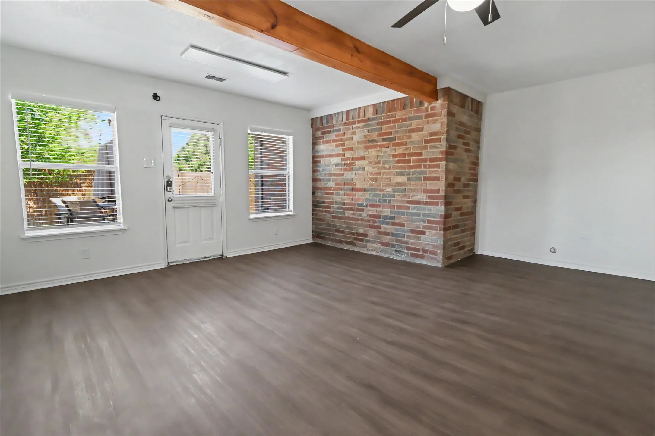 Spacious room featuring wood-finish flooring, a brick accent wall, and a rustic wood ceiling beam