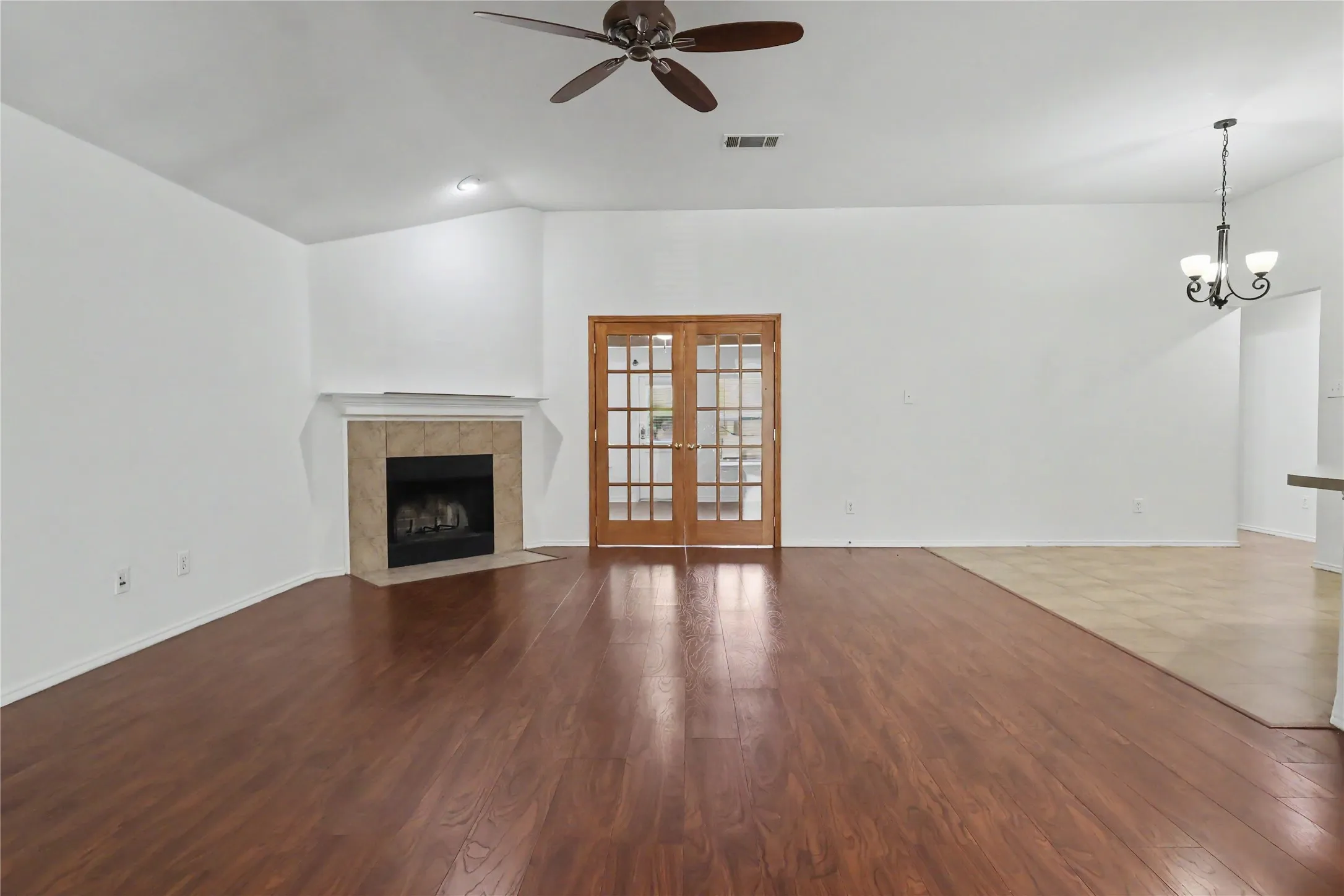 Spacious living area featuring wood-finish flooring, a corner fireplace with a tile surround and mantel, and French doors