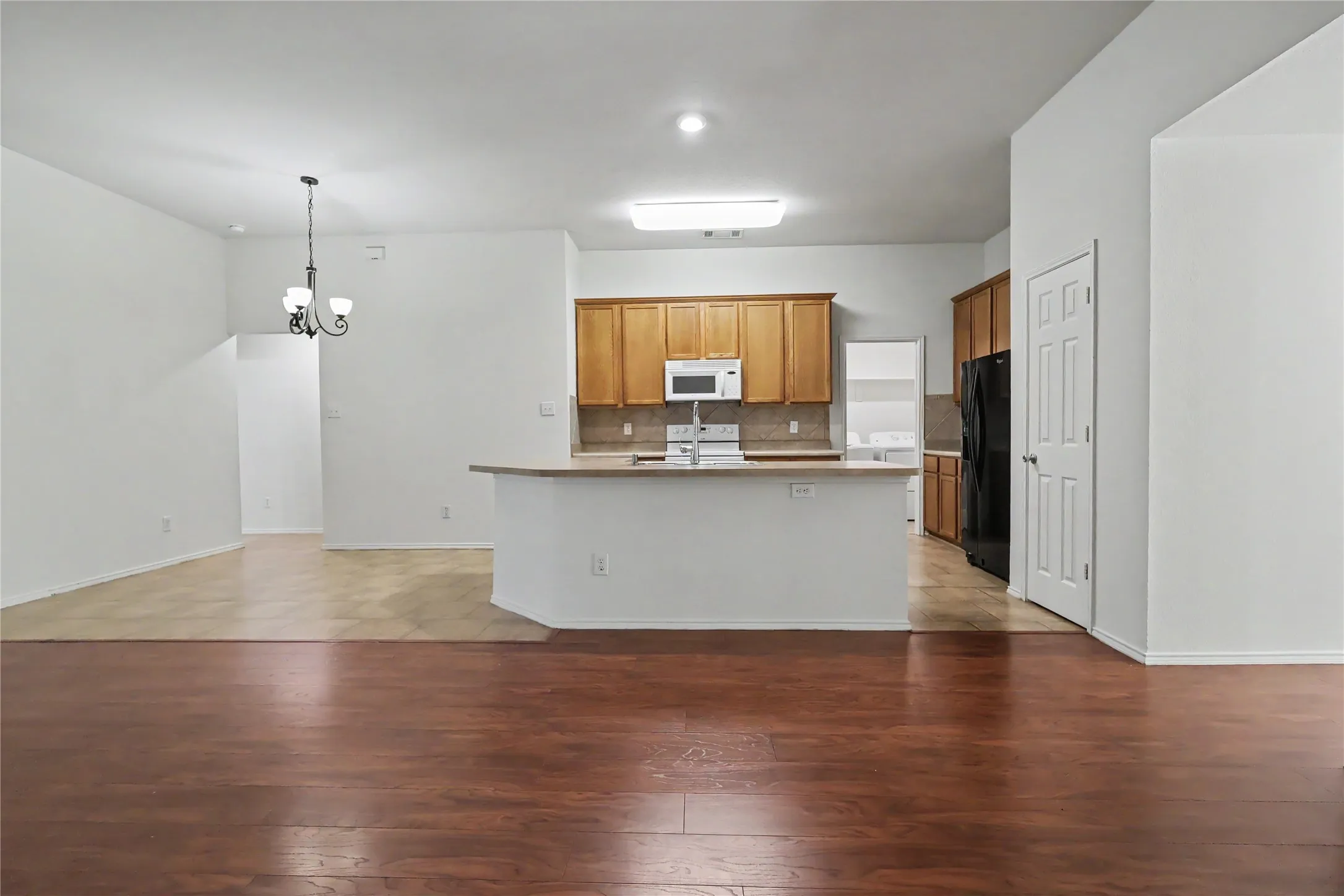 Open-concept living space featuring wood-finish flooring, a kitchen island with sink, wood cabinetry, built-in microwave, and a black refrigerator