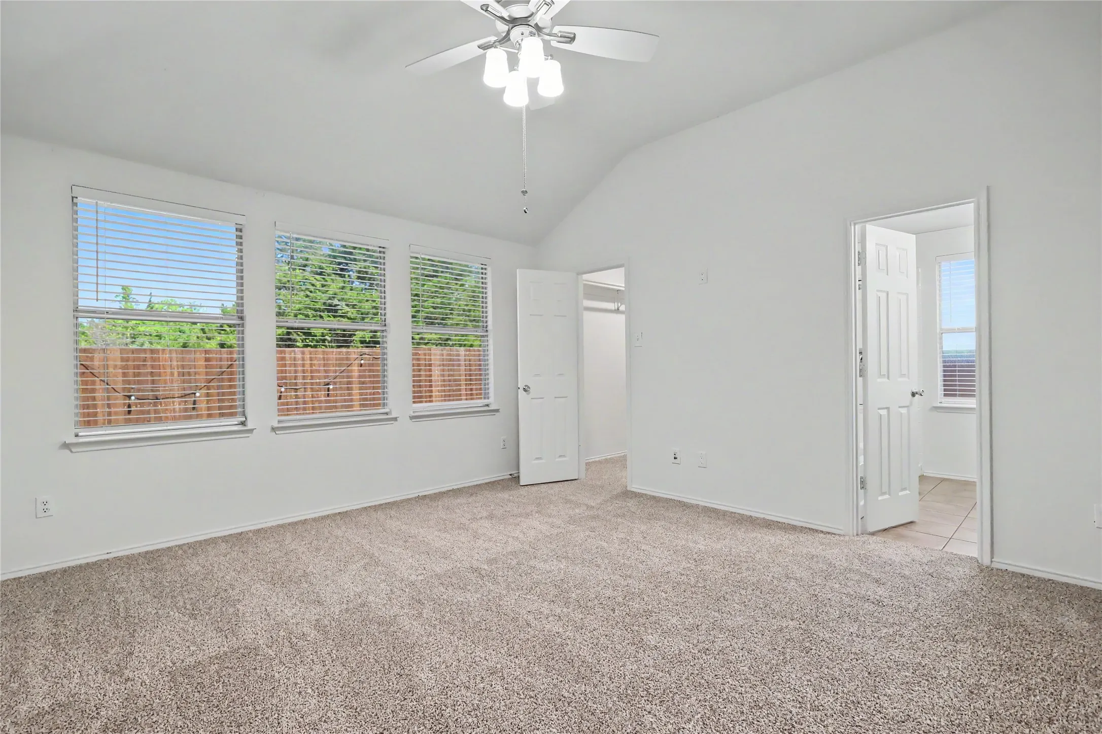 Carpeted room featuring a vaulted ceiling and a ceiling fan with integrated lighting