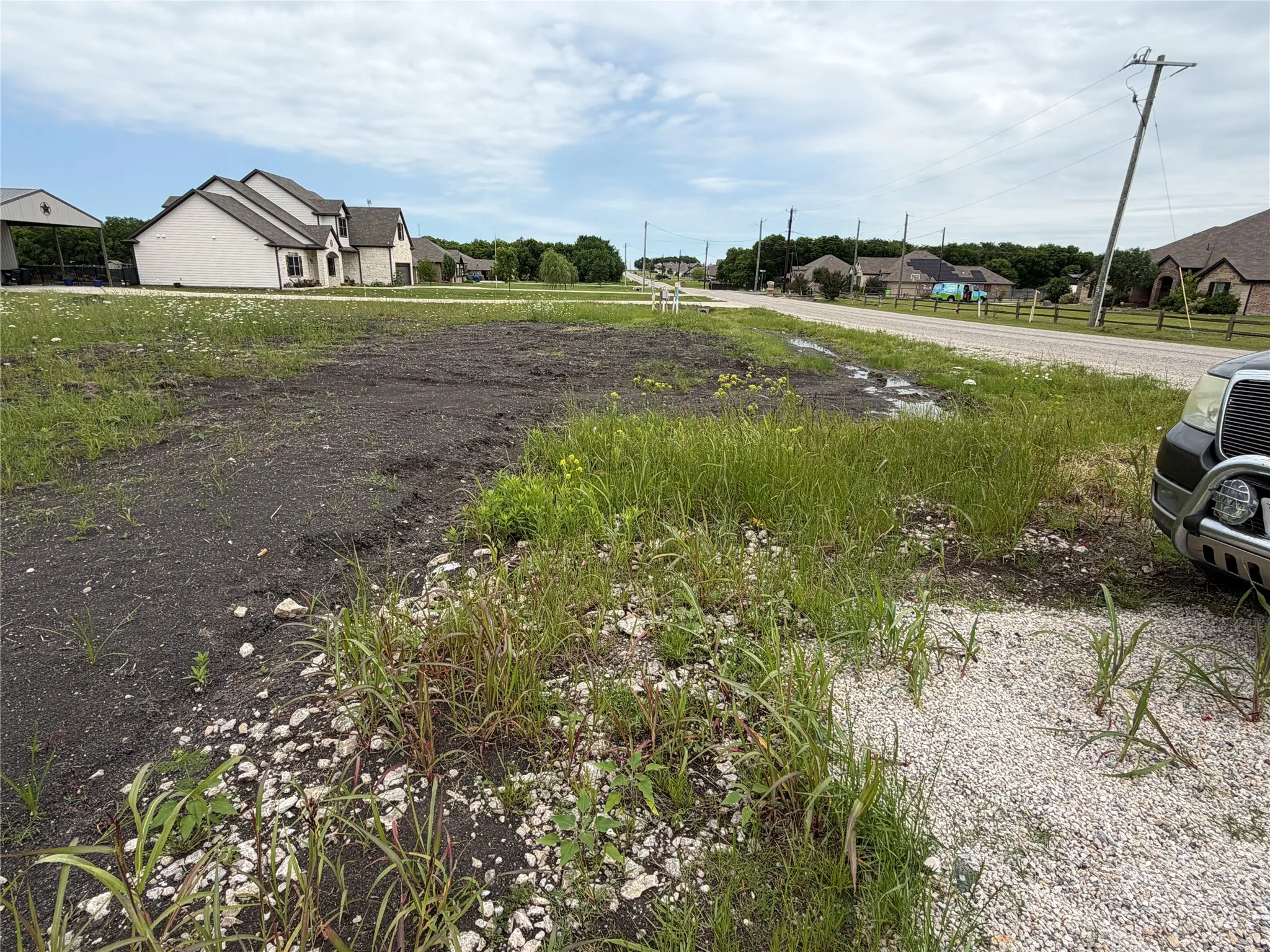 Expansive undeveloped lot featuring mixed terrain with dark soil, scattered vegetation, and partial gravel coverage