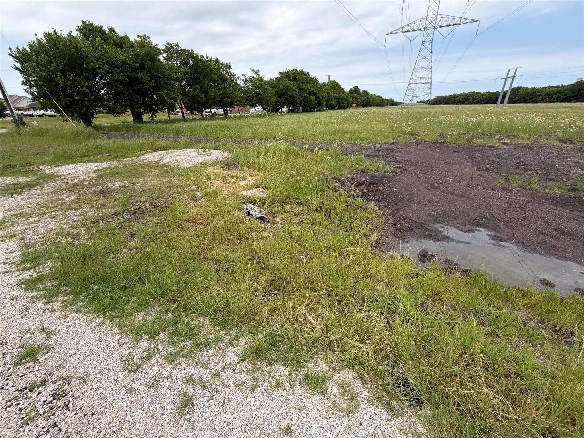 Expansive parcel featuring a power line structure, gravel surfacing, and a mix of grass and dirt ground cover
