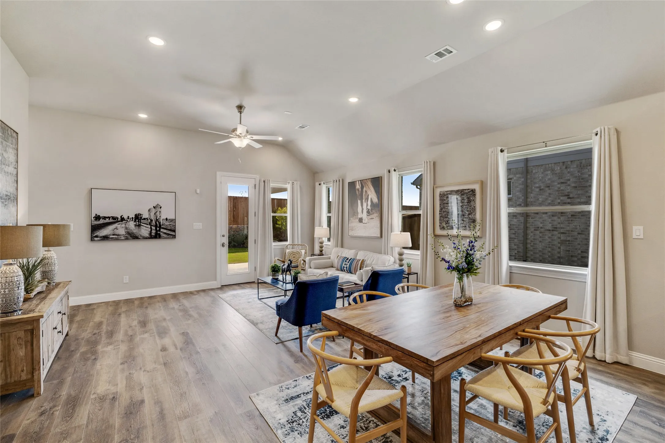 Open-concept living and dining area featuring wood-finish flooring, recessed lighting, and a vaulted ceiling