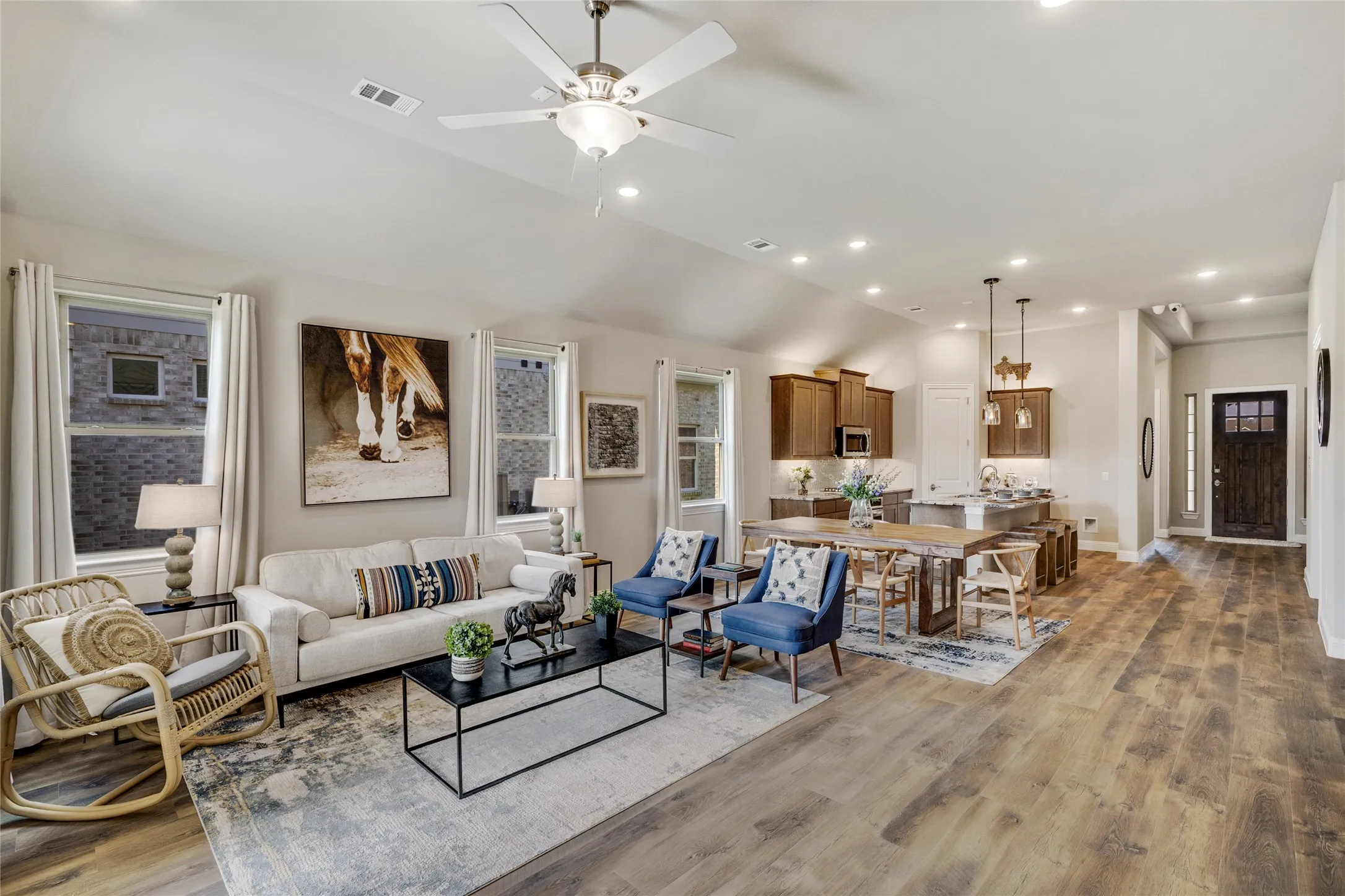 Expansive open-concept living area featuring wood-finish flooring, vaulted ceilings with a ceiling fan, and recessed lighting