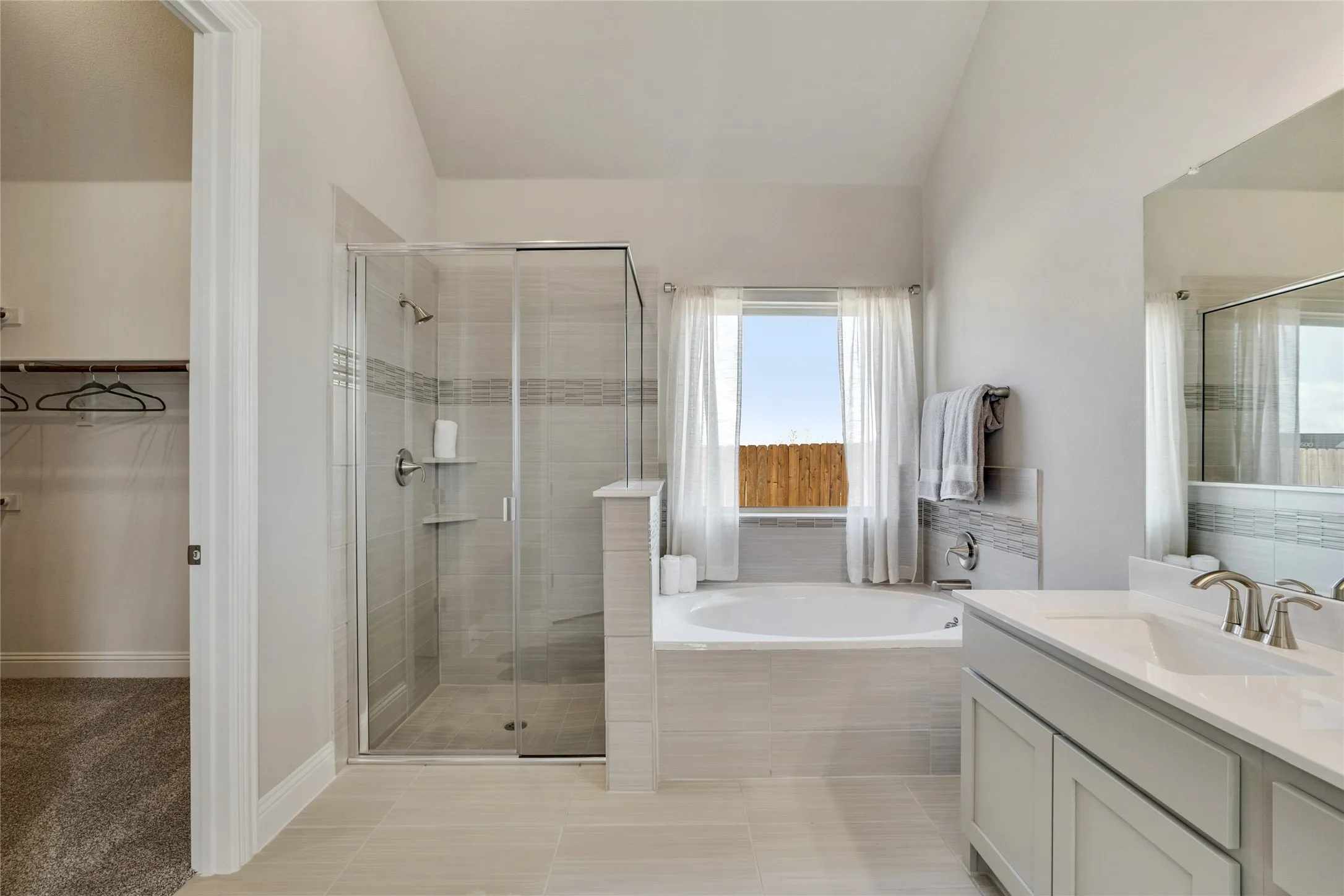 Spacious bathroom featuring a glass-enclosed shower, a built-in soaking tub under a window, and a dual-sink vanity with a quartz-finish countertop