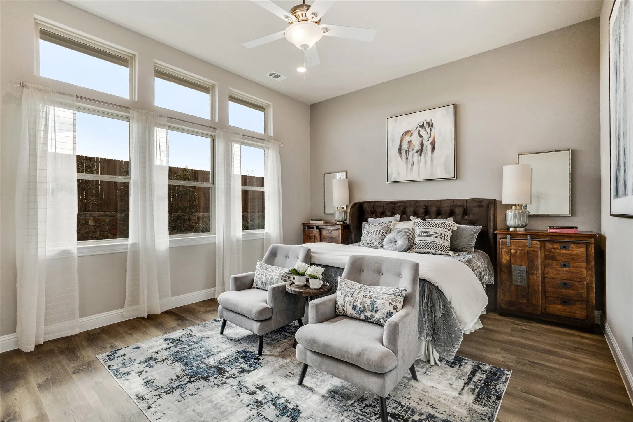 Spacious room featuring wood-finish flooring, a ceiling fan with integrated lighting, and multiple large windows with transom panels