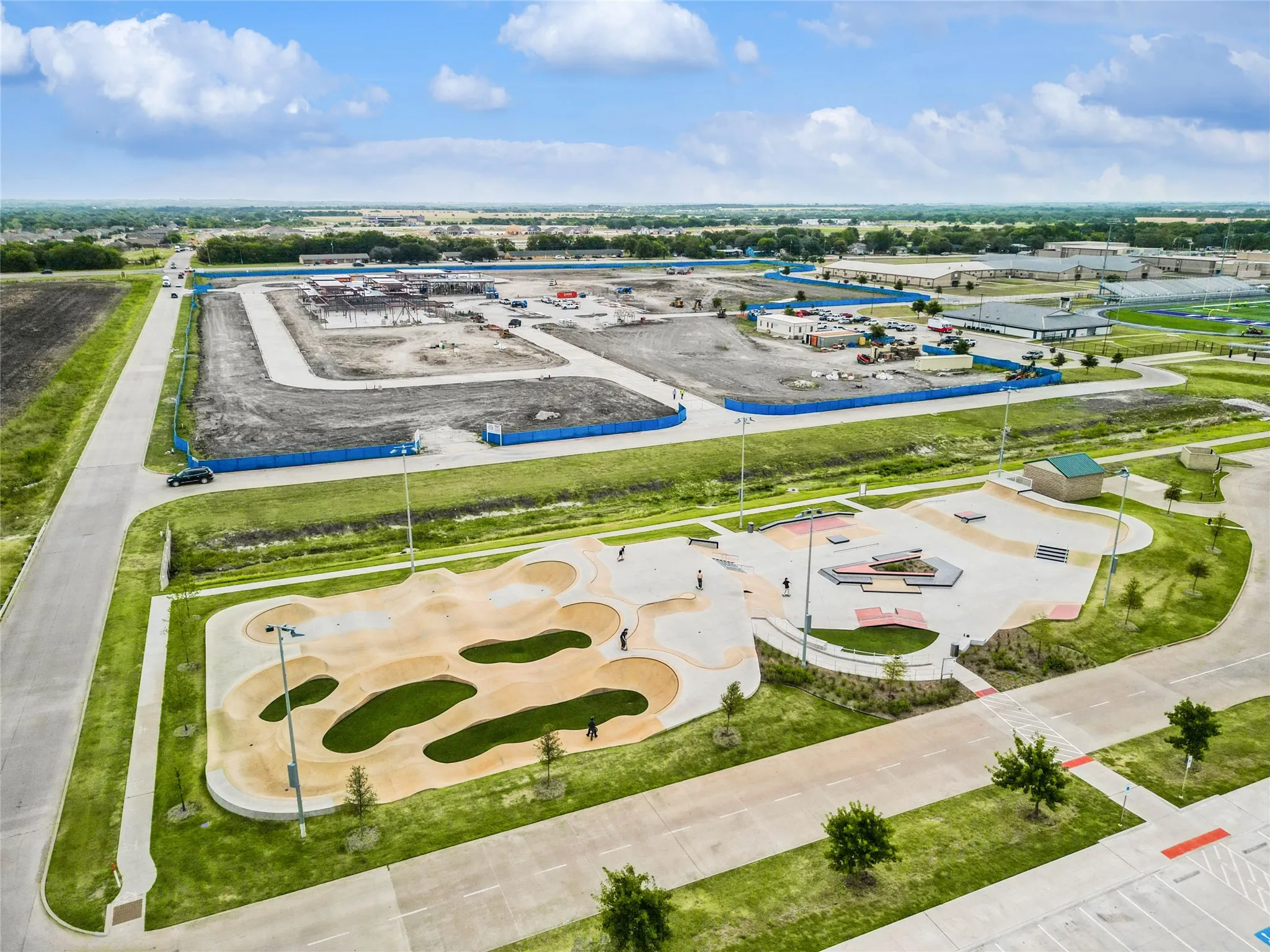 Aerial perspective showcasing a modern skatepark with multiple concrete bowls and ramps, surrounded by green spaces