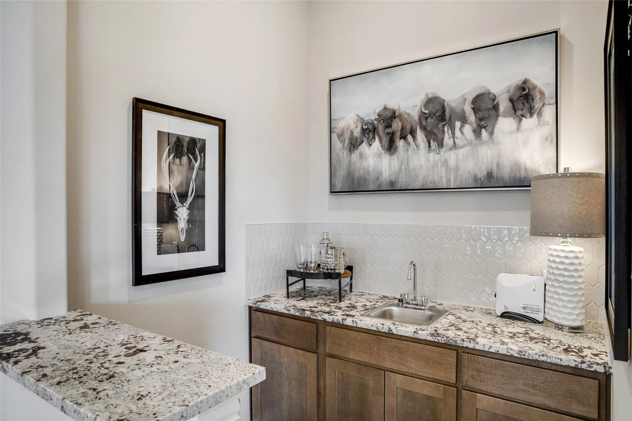 Wet bar featuring granite countertops, a stainless steel sink, wood-finish cabinetry, and a white patterned tile backsplash