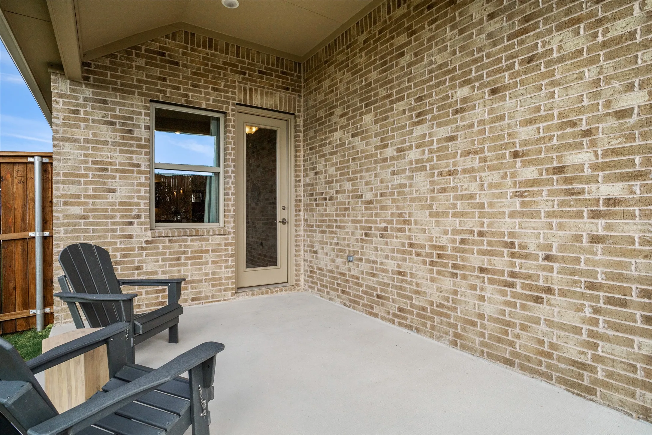Covered patio featuring a concrete slab, brick exterior, and a privacy fence