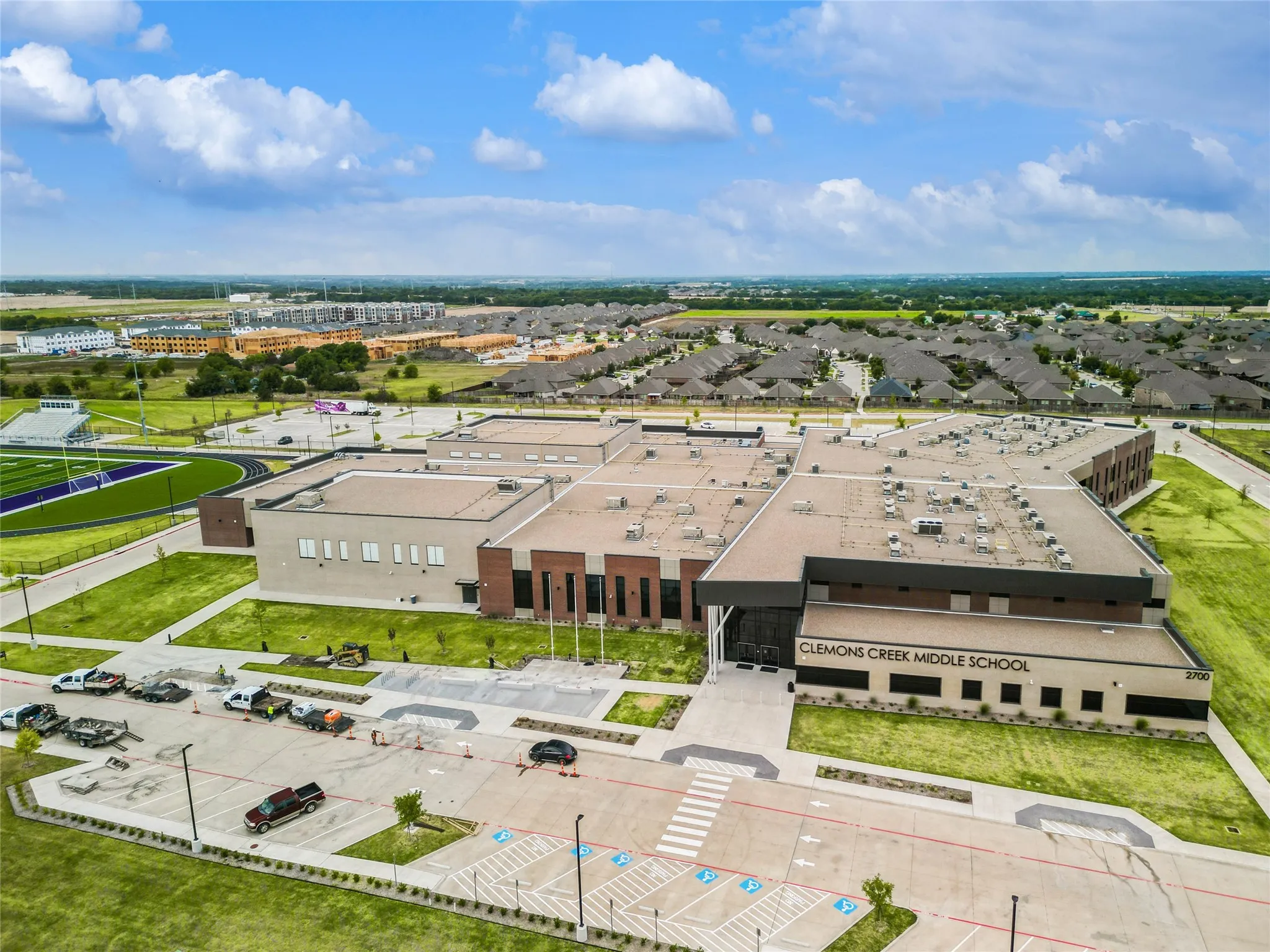 Expansive campus featuring a multi-story building with brick and stucco exterior, a large parking area, a track and field stadium with bleachers, and surrounding residential neighborhoods