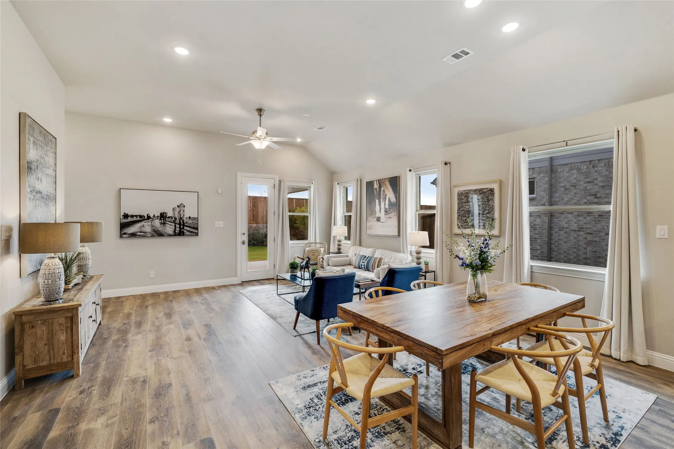 Open-concept living and dining area featuring wood-finish flooring, recessed lighting, and a vaulted ceiling