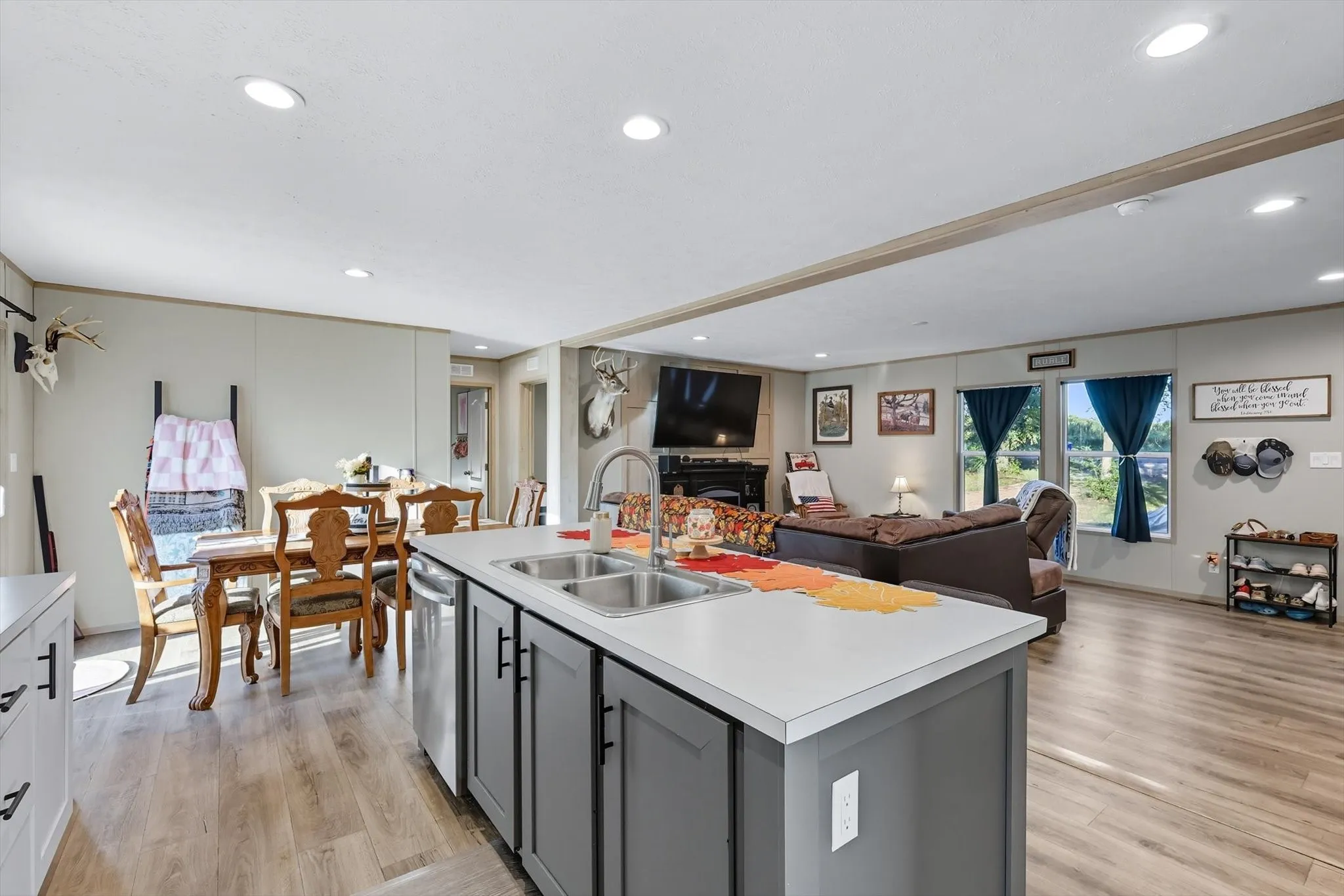Kitchen with gray cabinetry, open floor plan, light countertops, light wood-style floors, and a kitchen island with sink