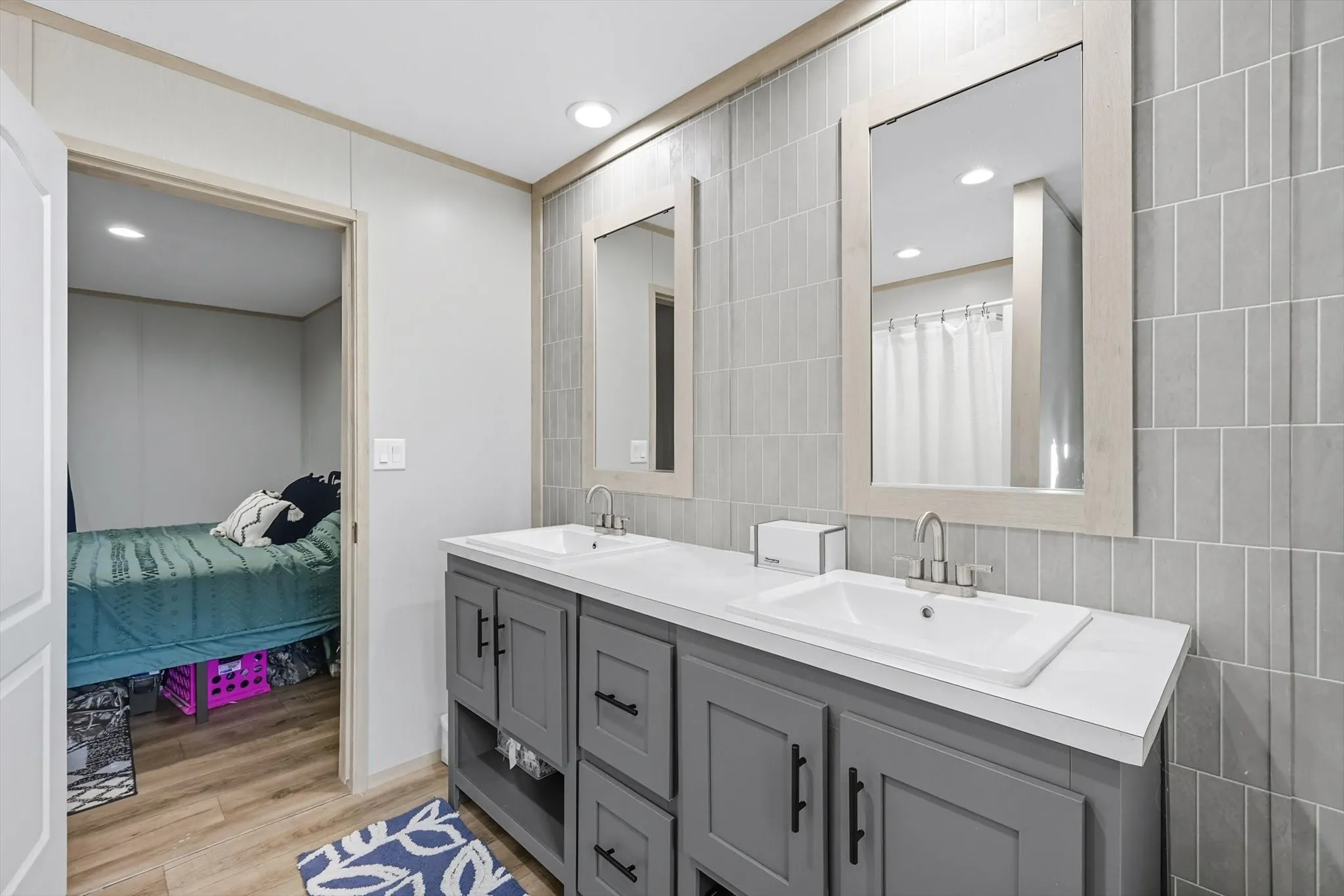 Ensuite bathroom featuring light wood finished floors, recessed lighting, double vanity, and tile walls