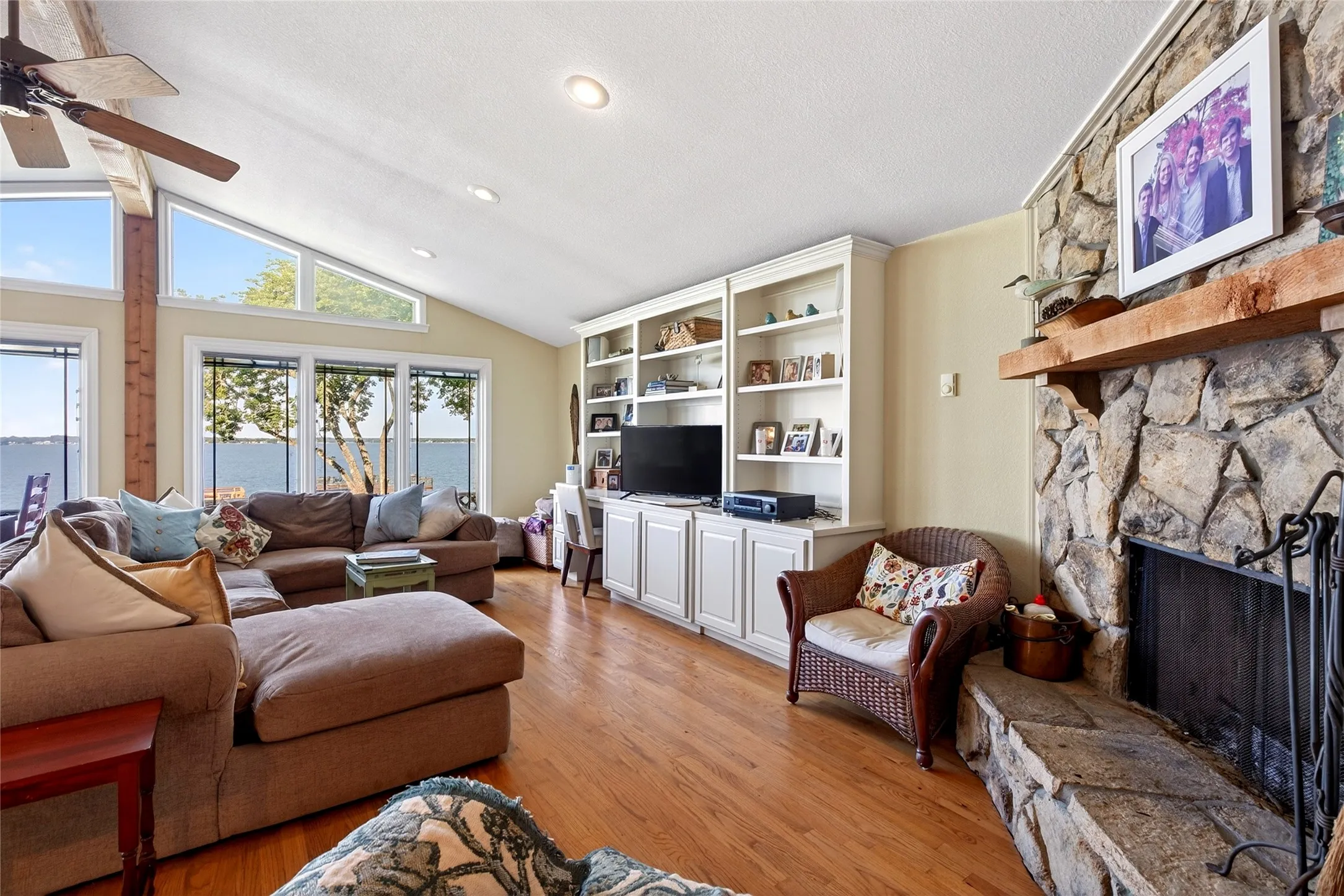 Spacious living area featuring expansive windows, it is hard to take your eyes off that WOW view, a vaulted ceiling, oak hardwood floor, a stone wood burning fireplace with wood mantel, and built-in cabinetry with shelving