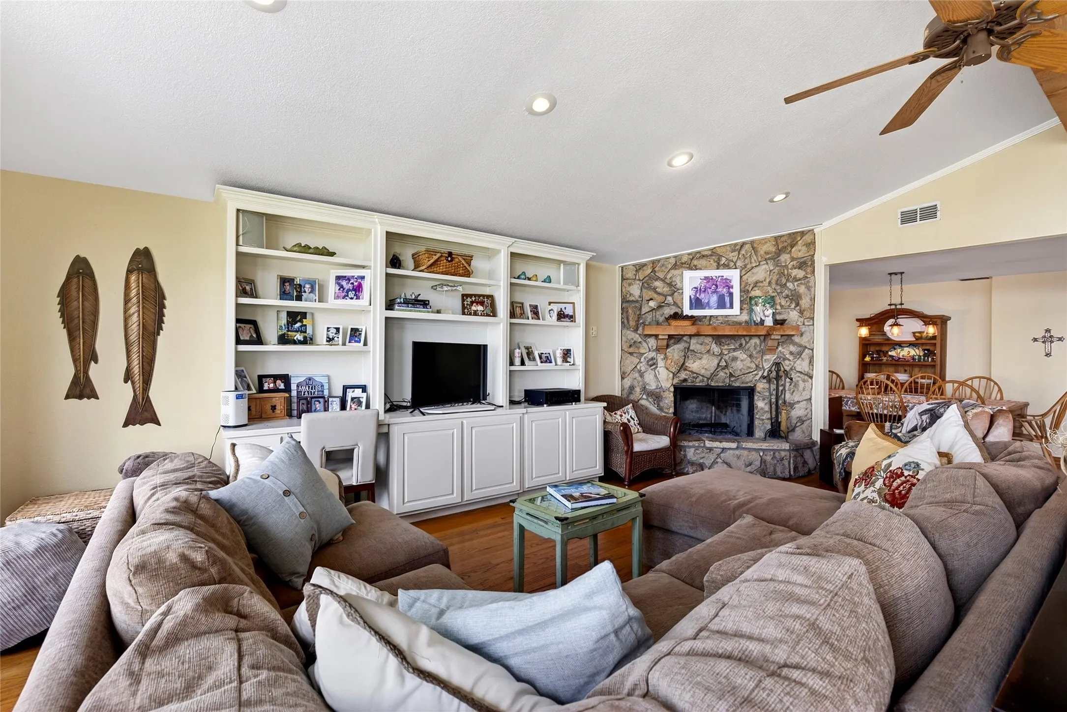 Living space featuring a stone wood burning fireplace with a wood-finish mantel, built-in shelving with lower cabinetry, oak hardwood flooring, and recessed lighting.  While conversing with friends, your eyes won't leave the amazing water view out the windows.
