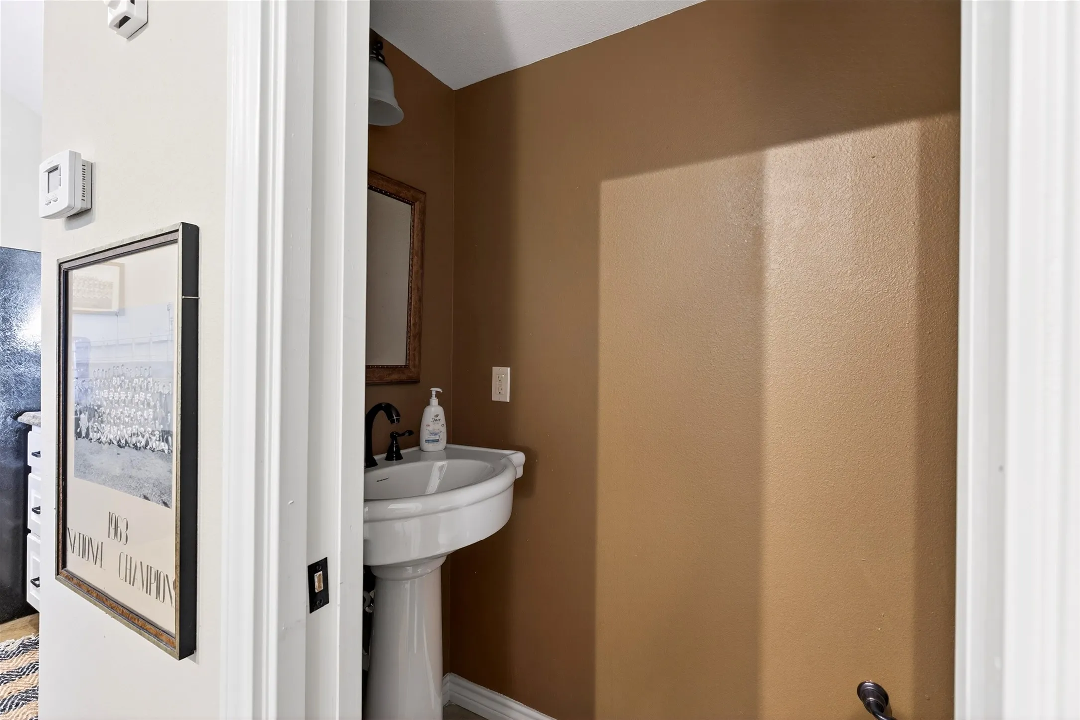 Cabin 2nd Half Bath off of the living space features a pedestal sink with black faucet, complemented by a framed mirror and overhead lighting fixture, set against warm-toned walls.