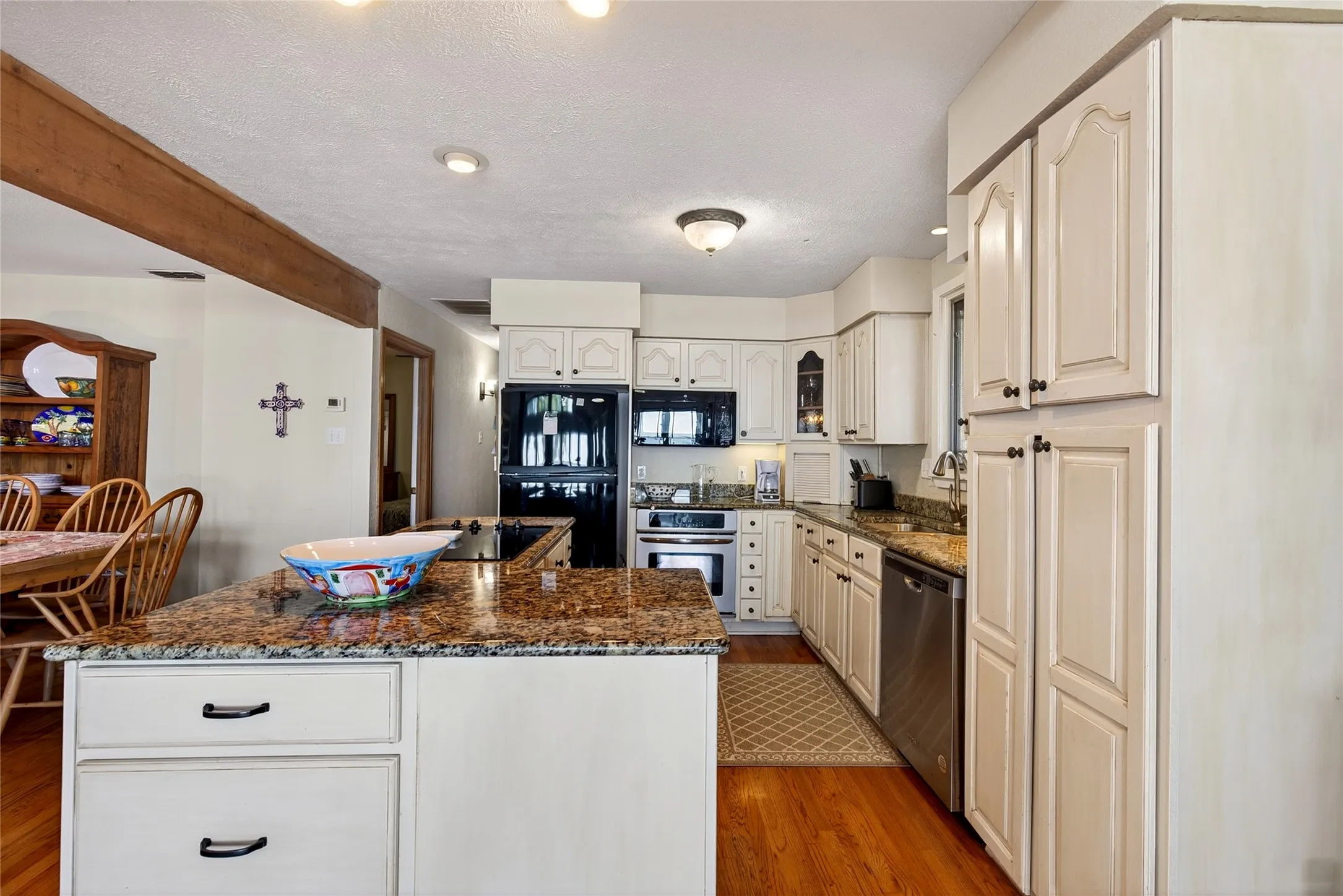 Kitchen featuring a central island with granite countertop, cabinetry, stainless steel appliances and dishwasher, and oak hardwood flooring.