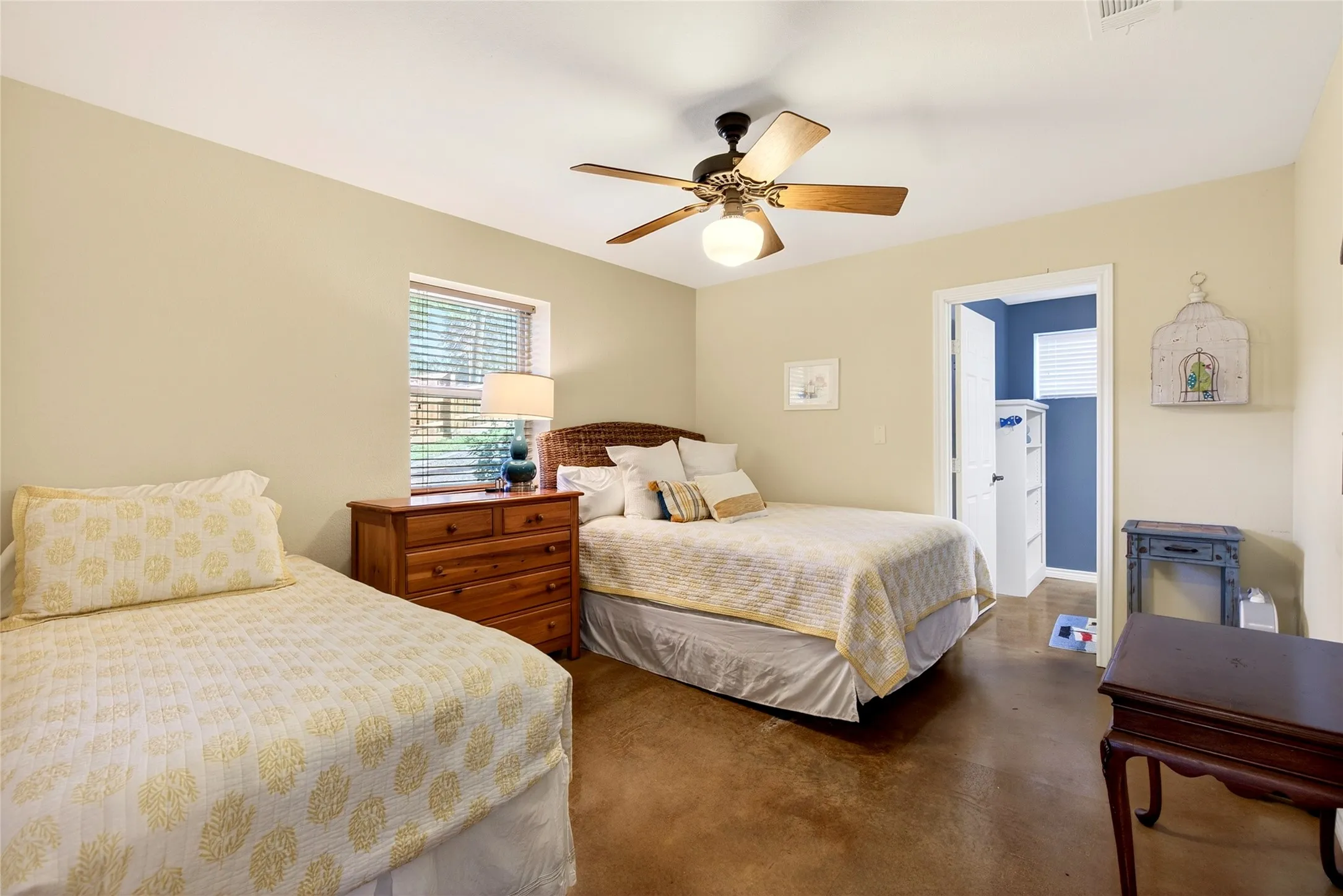 Cabin Bedroom #2 featuring a ceiling fan with integrated lighting, a window with blinds, and durable stained concrete flooring, and ensuite half bath.