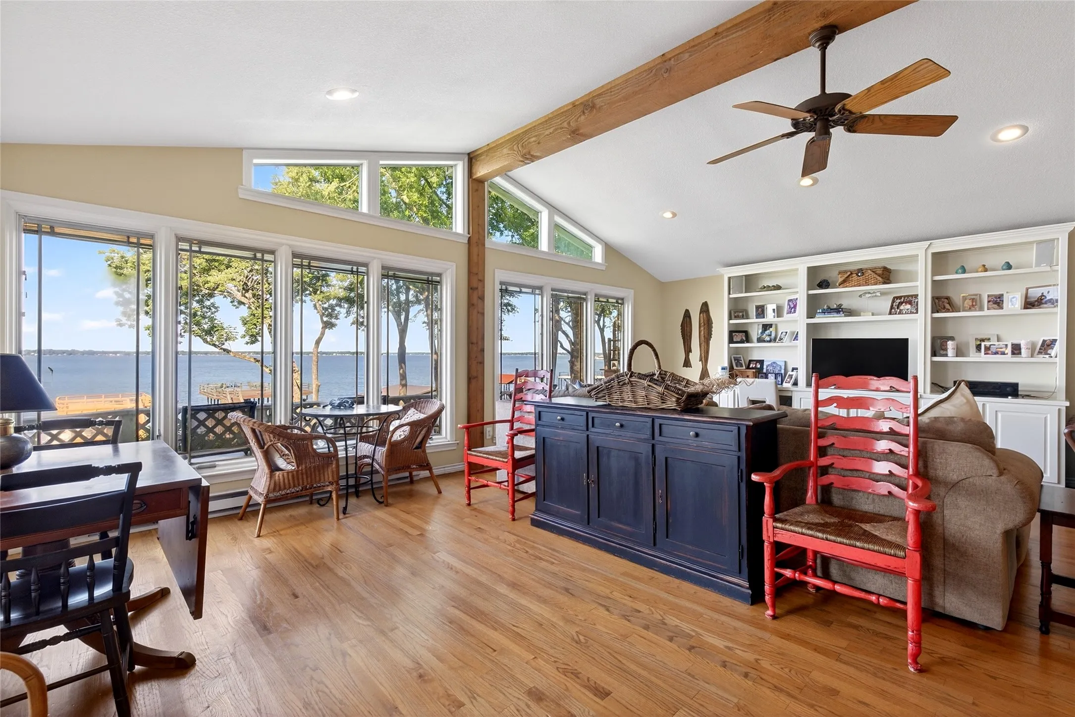 Great room featuring expansive waterside windows, Oak hardwood floors, vaulted ceiling with exposed wood beams, a built-in media center with shelving, and a wood burning fireplace.