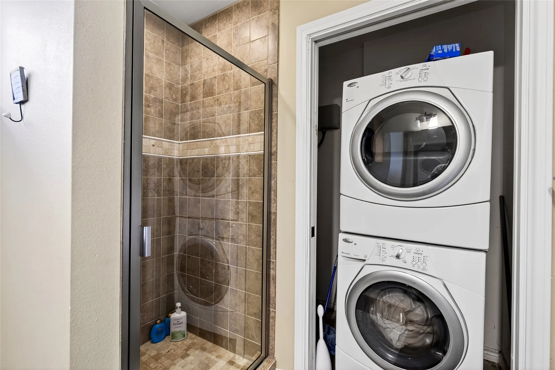 Cabin full bathroom Shower enclosure with glass door and tile surround featuring an accent tile band and stackable washer and dryer.