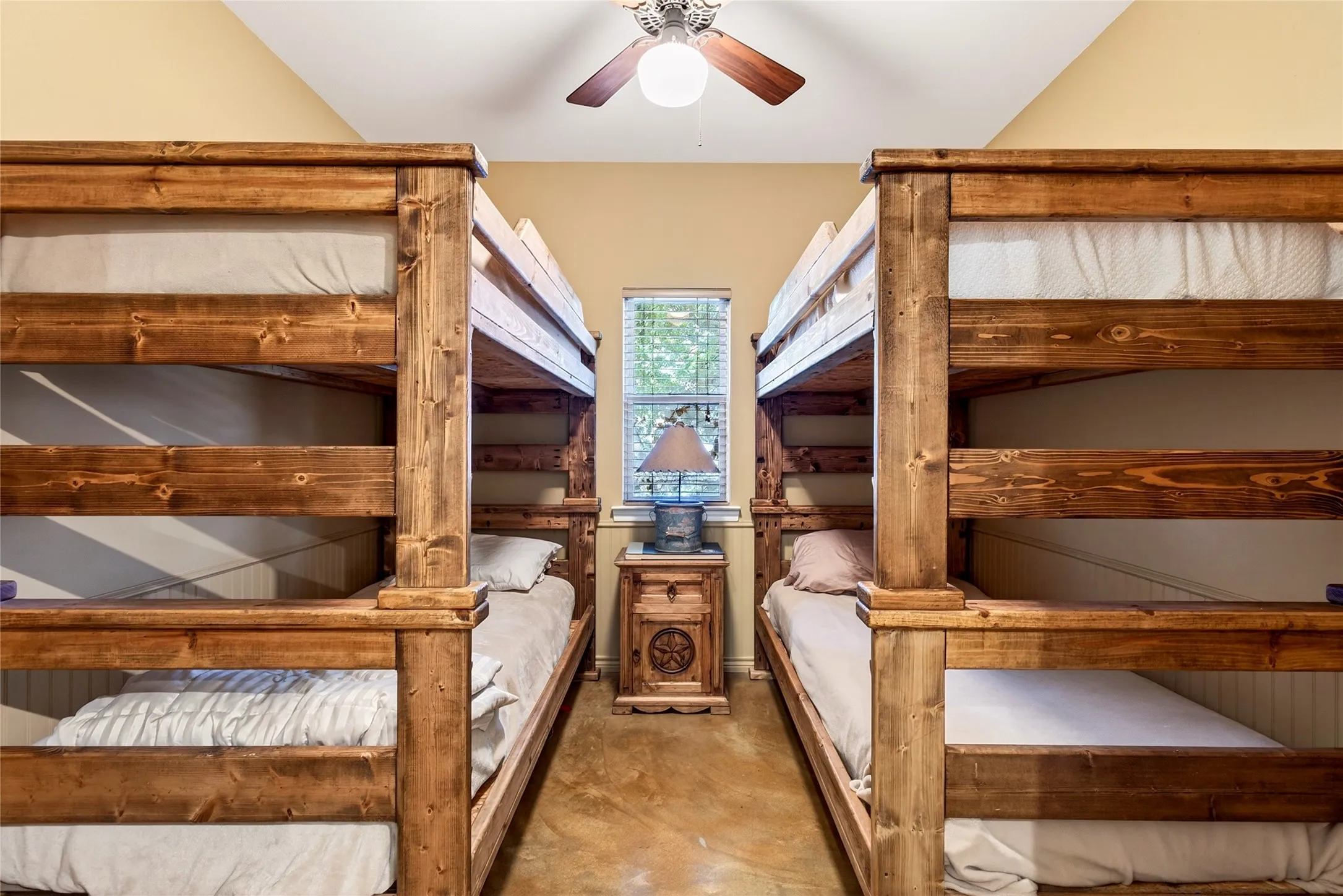 Cabin Bedroom#3 the Bunkroom featuring two wooden bunk bed structures (may be included), a window with natural light, a ceiling fan with integrated lighting, and concrete flooring