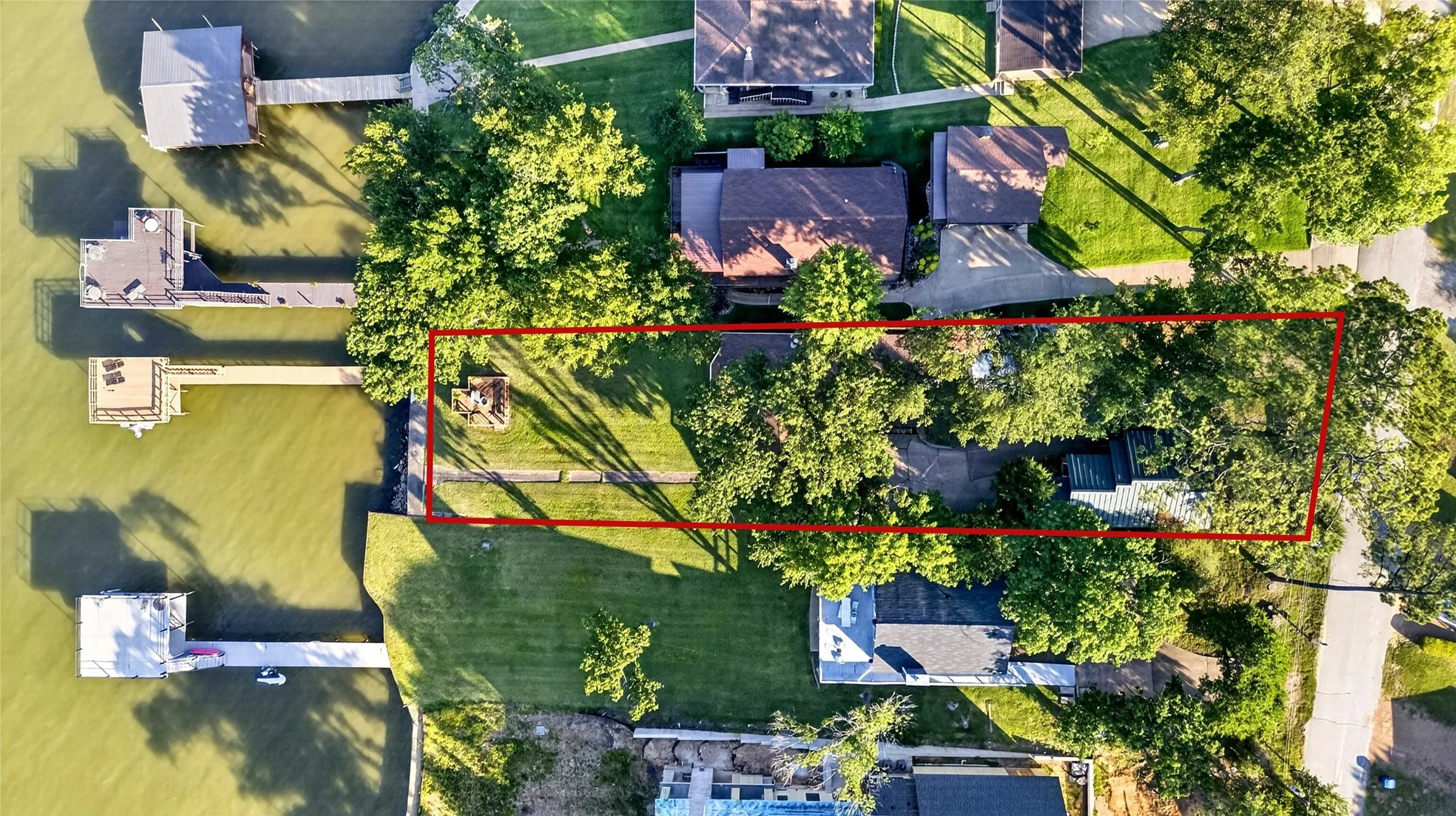 Waterfront property featuring extensive mature tree coverage, a private boat dock, mature shade trees and a manicured lawn.